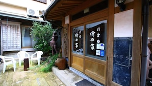 A traditional Japanese building with wooden sliding doors and a small outdoor seating area with plastic chairs.