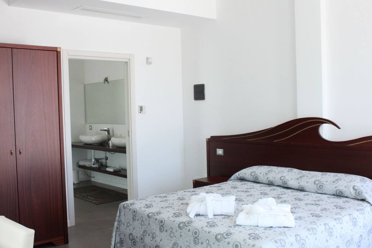 A bedroom with a wooden headboard, a bed with patterned bedding, and a bathroom visible through an open door.