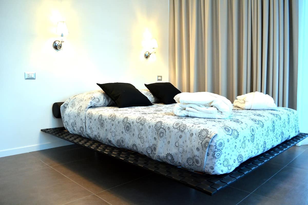 A modern bedroom with a large bed, two wall-mounted lamps, and a view of the outside through curtains.