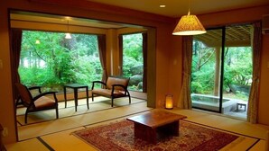 A room with tatami flooring, a low wooden table, two chairs, and a large sliding glass door leading to a garden. - Soranoniwa Petit Hotel (Nihommatsu)