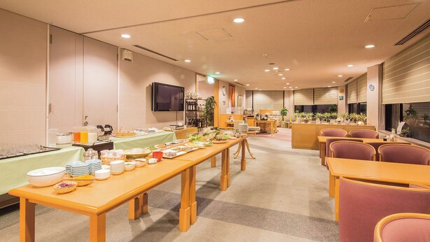 A spacious dining area with multiple tables and chairs, a buffet setup, and a television mounted on the wall. - Urban Hotel Nishiwaki (Nishiwaki)