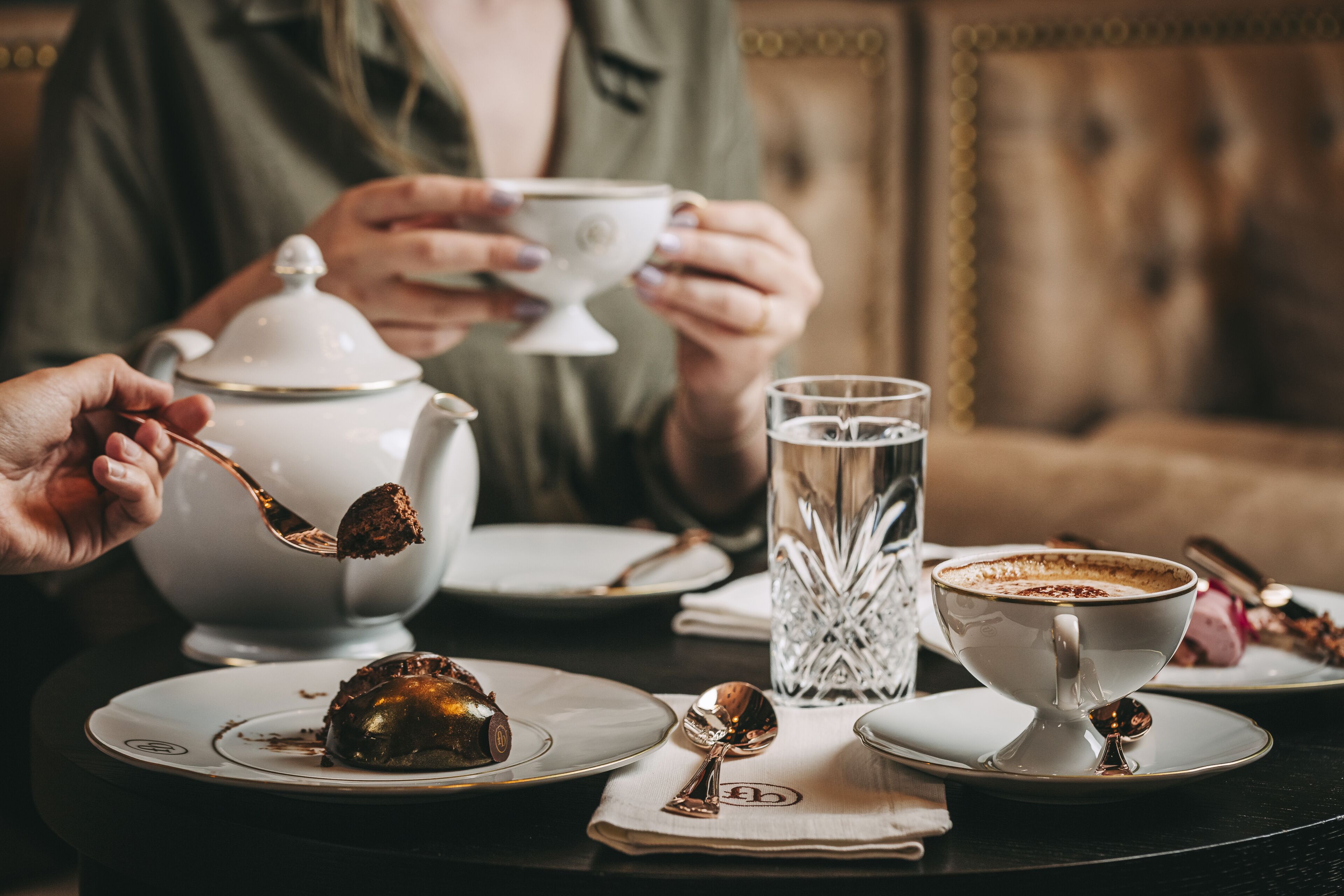 A dining table with a dessert, a teapot, a cup of coffee, and a glass of water.