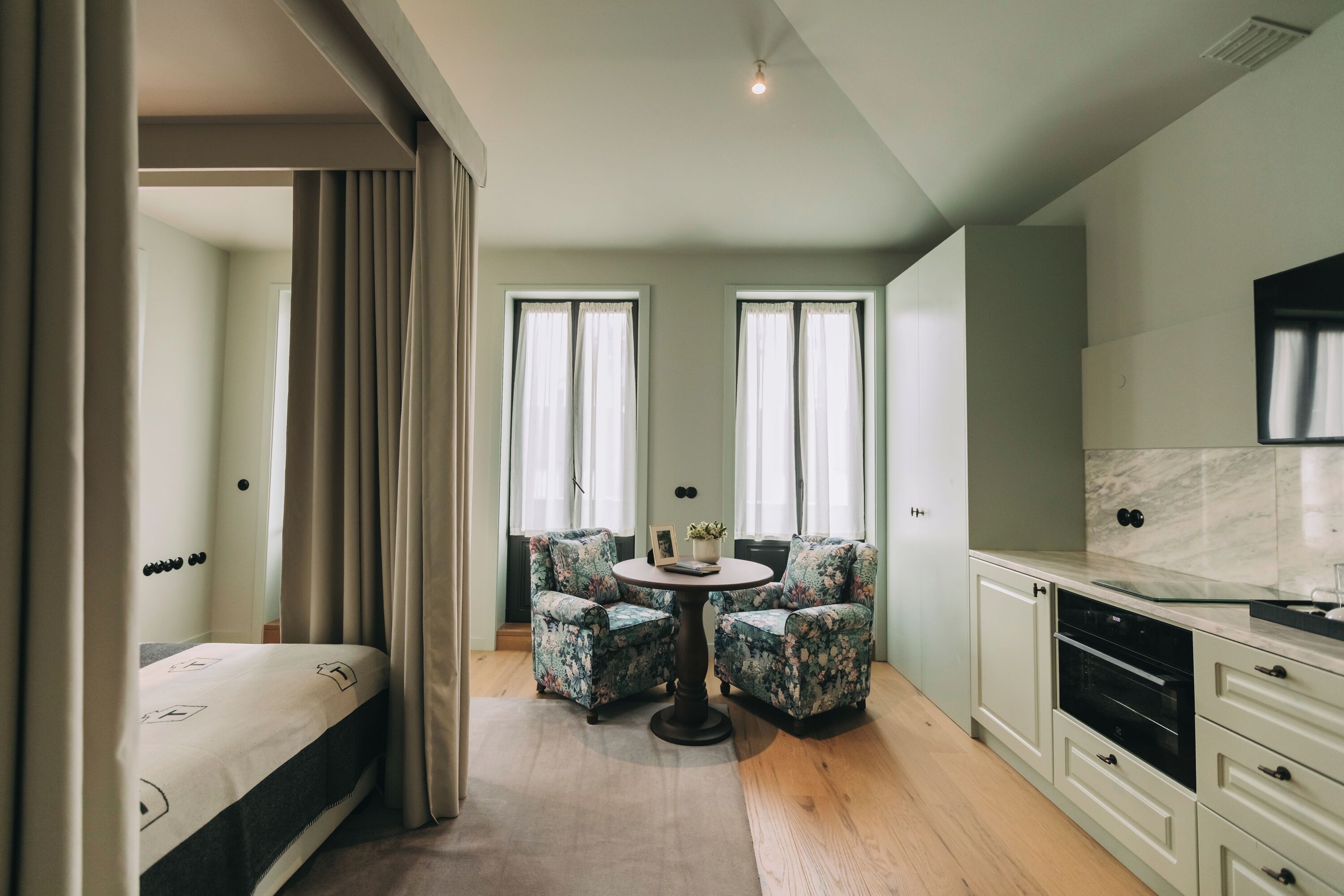 Ein gemütlicher Raum mit einem Bett, einem runden Tisch mit Stühlen, einer Küchenzeile und einem großen Fenster.