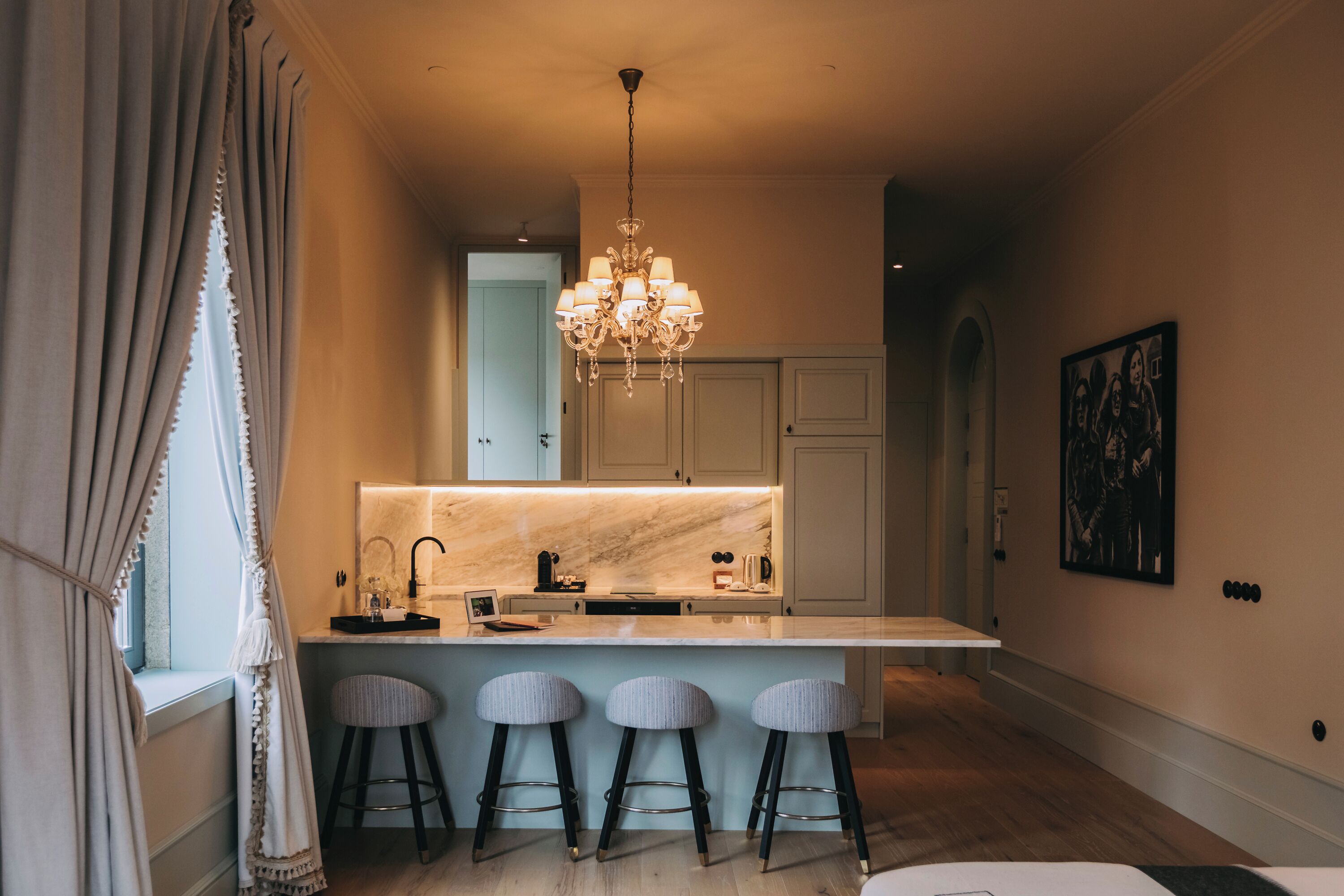A modern kitchen with a marble countertop, a chandelier, and three bar stools.