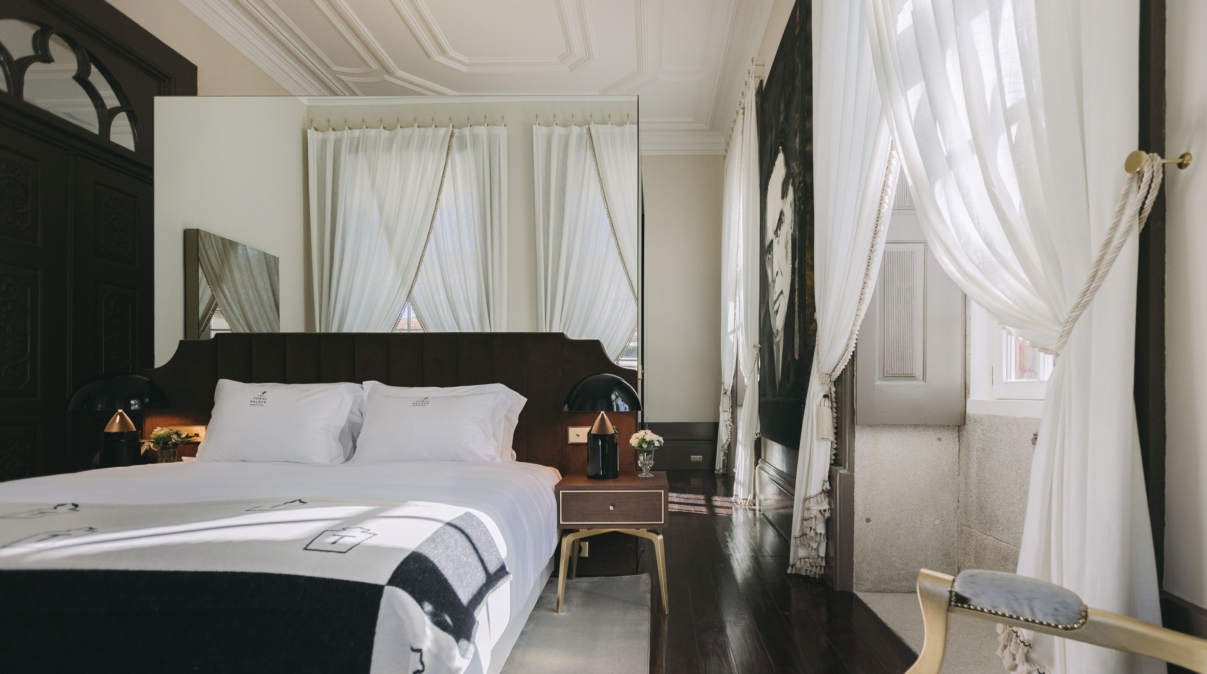 A hotel room with a large bed, a nightstand, a chair, and a large mirror.