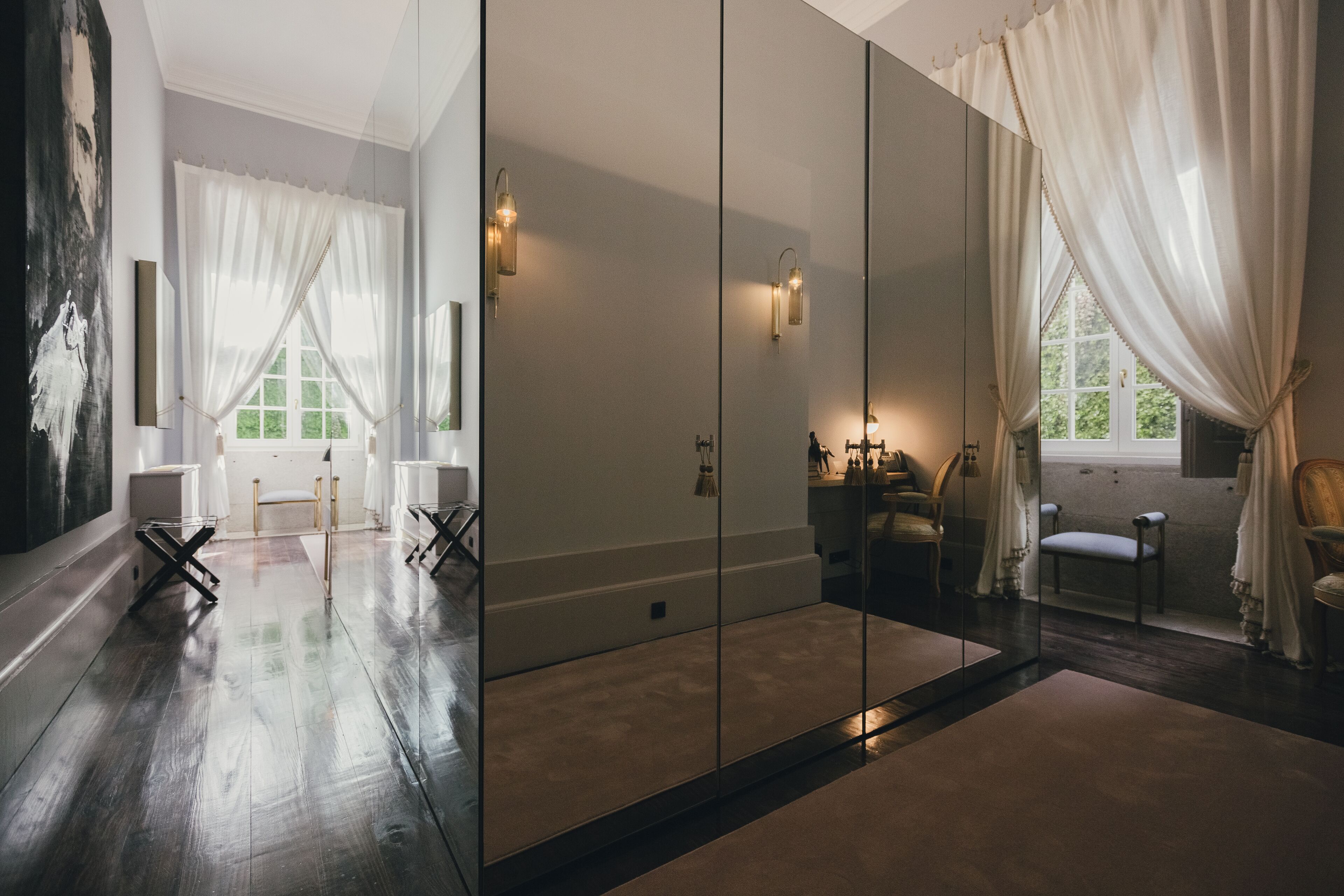 A spacious room with a large mirror, a wooden floor, and a view of a green landscape through a window.