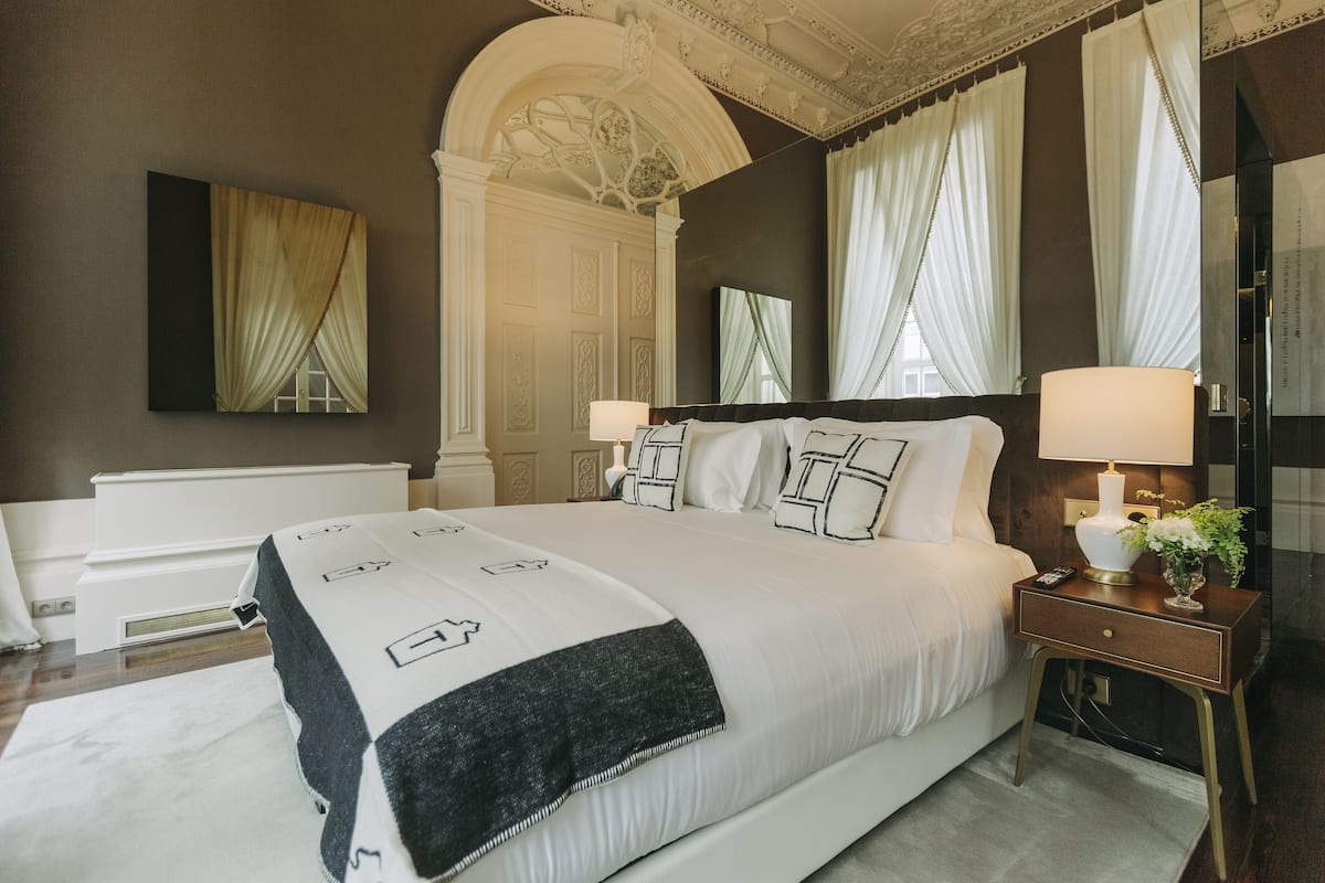 Un grand lit recouvert d’une couvre-lit noire et blanche, deux tables de chevet avec des lampes, un miroir et un panneau décoratif mural.