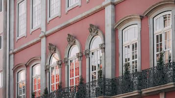 Fachada de edifício com janelas em arco, grades de metal ornamentadas e exterior rosado-avermelhado.