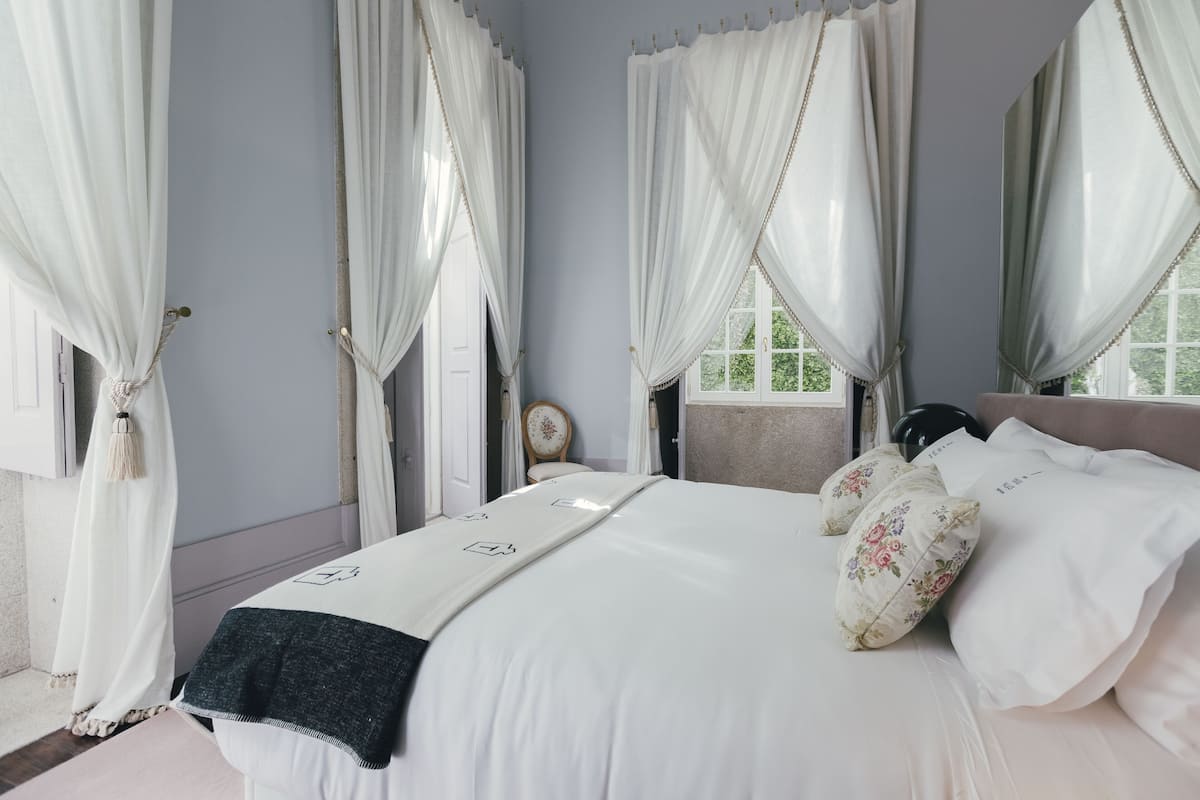 Une chambre à coucher avec un lit, des rideaux blancs et des coussins à motifs floraux.