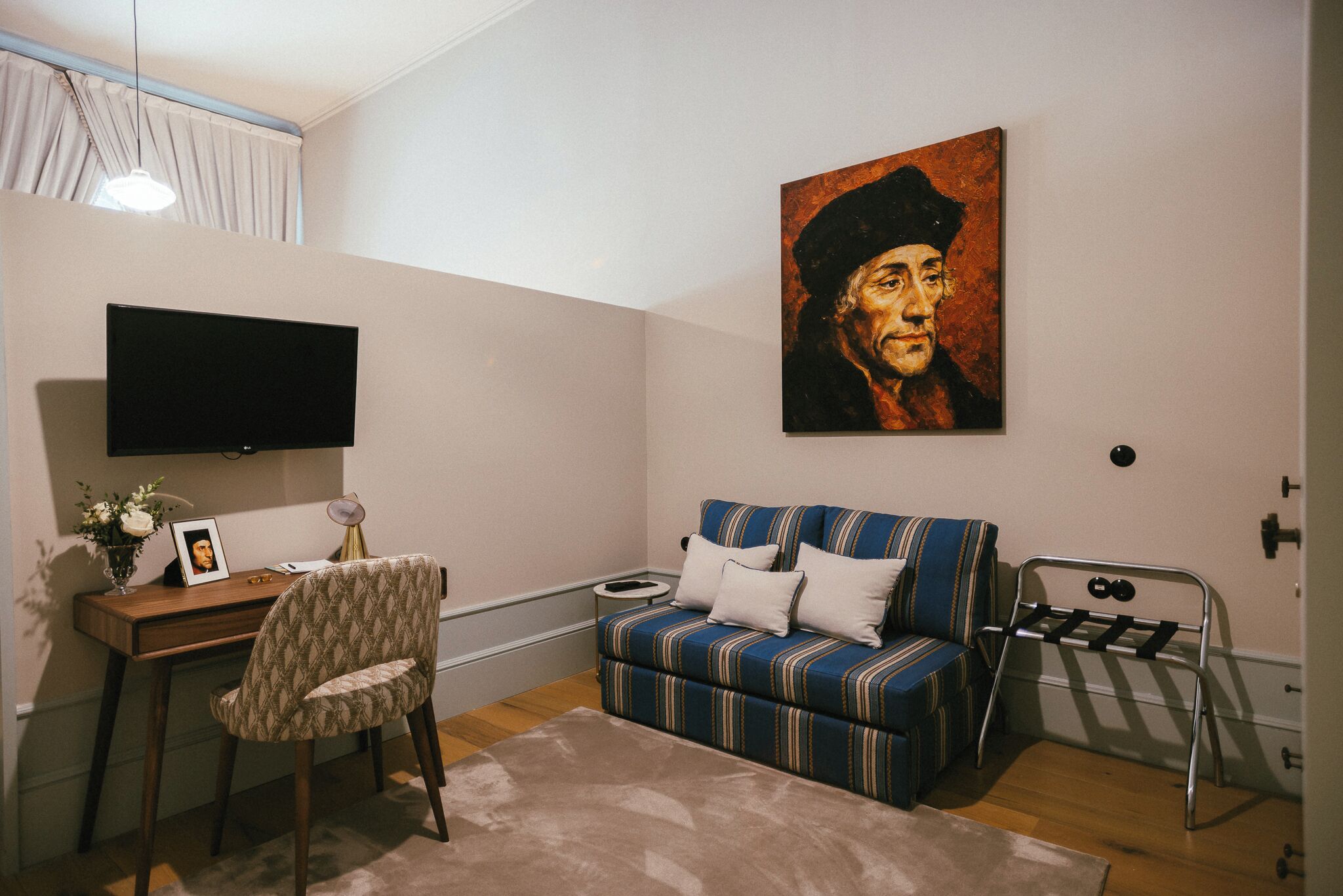 Una habitación con escritorio, silla, sofá, televisor, obras de arte y un radiador.