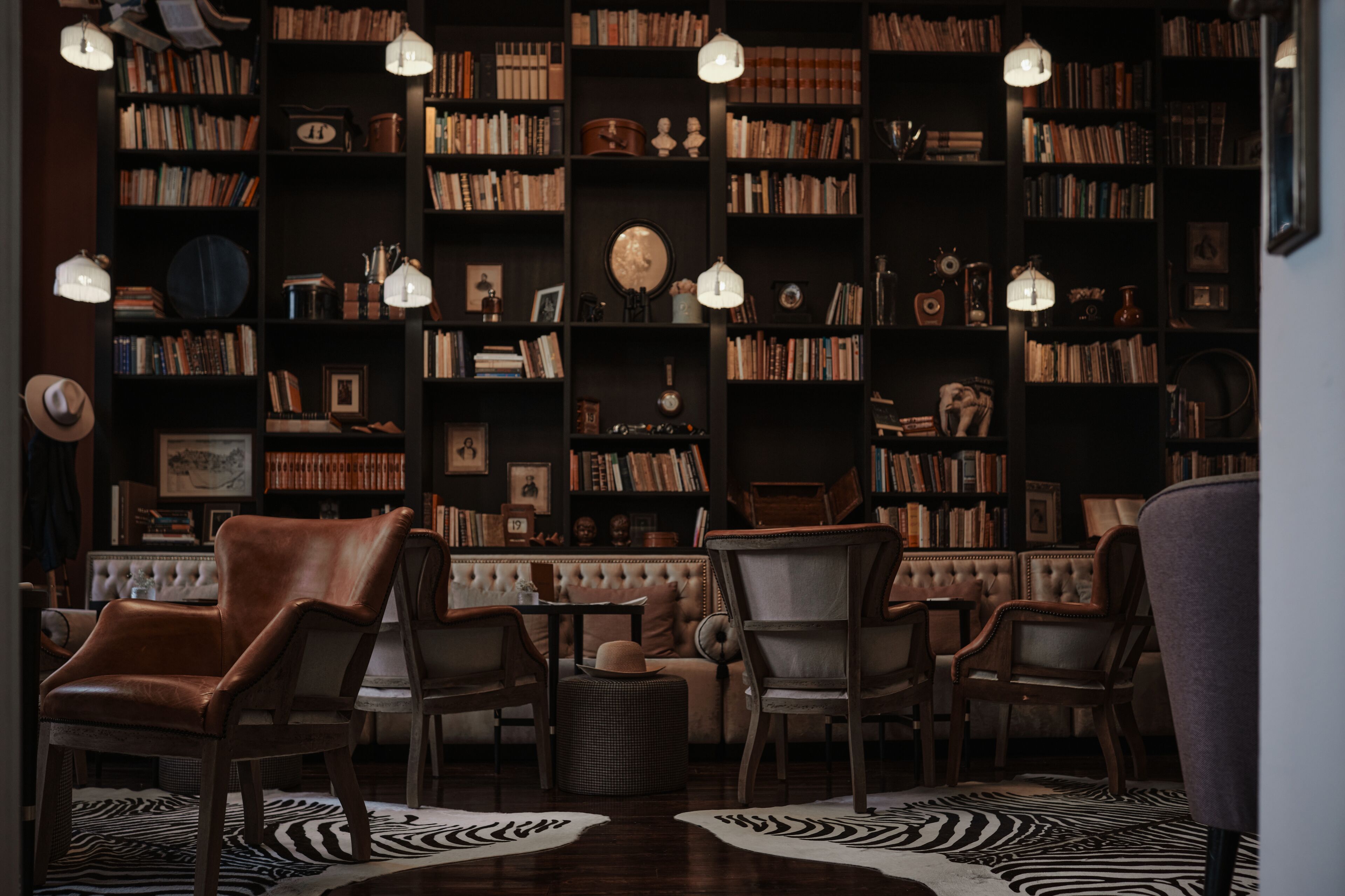 Una biblioteca acollidora amb butaques de cuir, un sofà amb respatller i un moqueta amb dibuix de zebra.