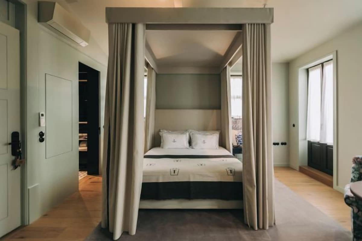A bedroom with a canopy bed, a wardrobe, and a view through a window.
