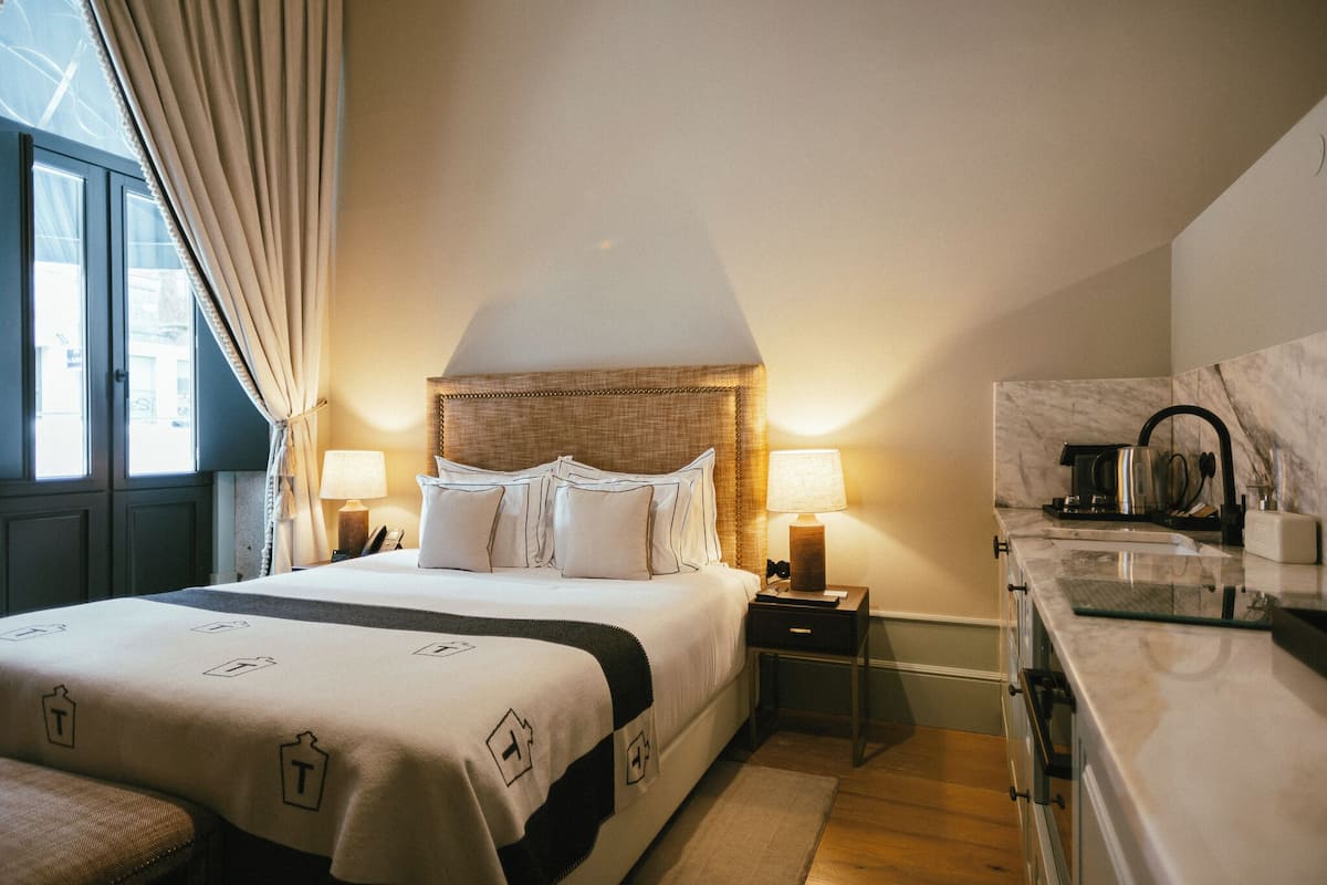 Une chambre d’hôtel avec un lit, des lampes de chevet, une table de nuit, un comptoir en marbre et une fenêtre avec des rideaux.