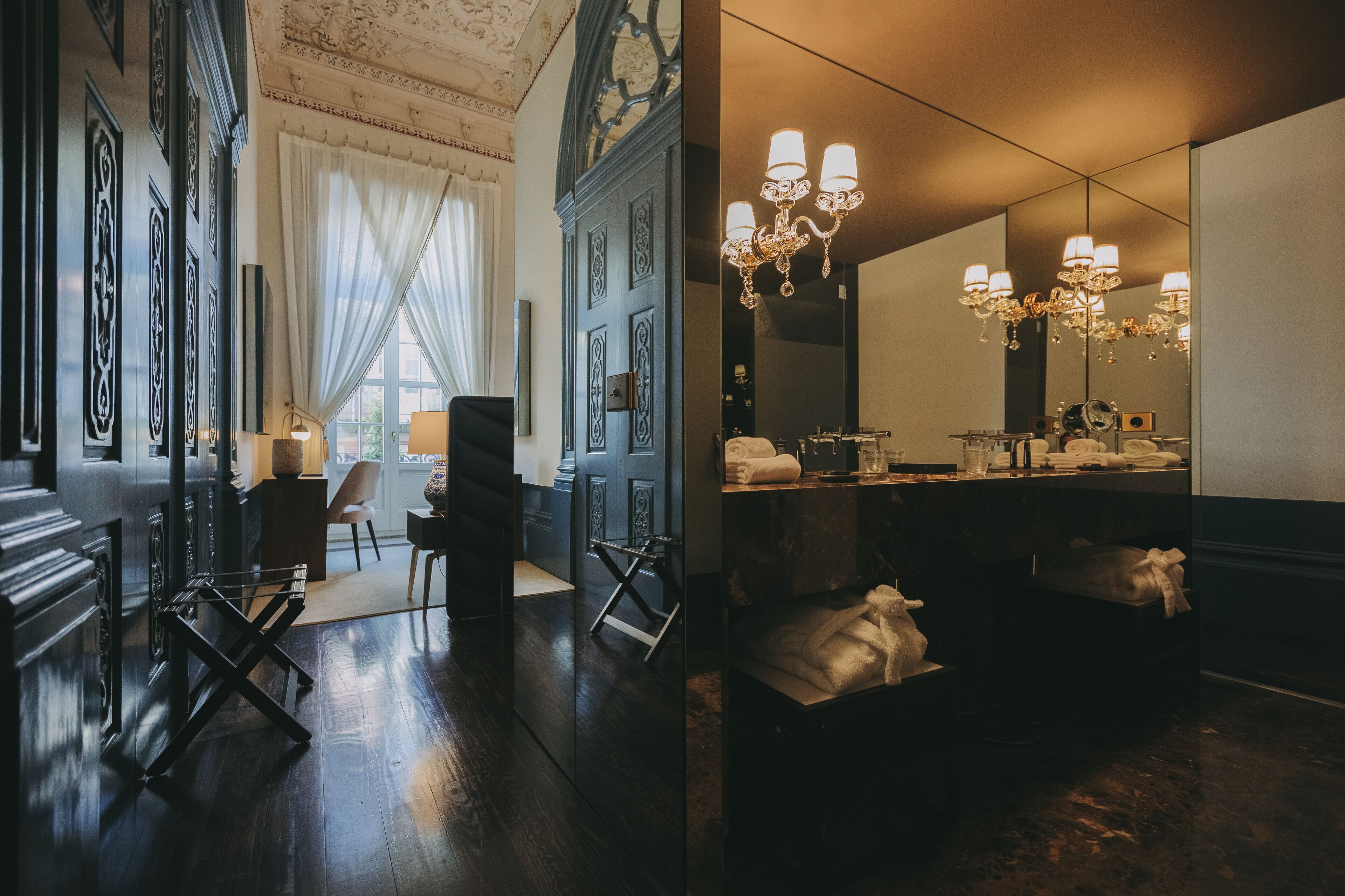 A luxurious bathroom with a large mirror, ornate wall panels, and a chandelier.