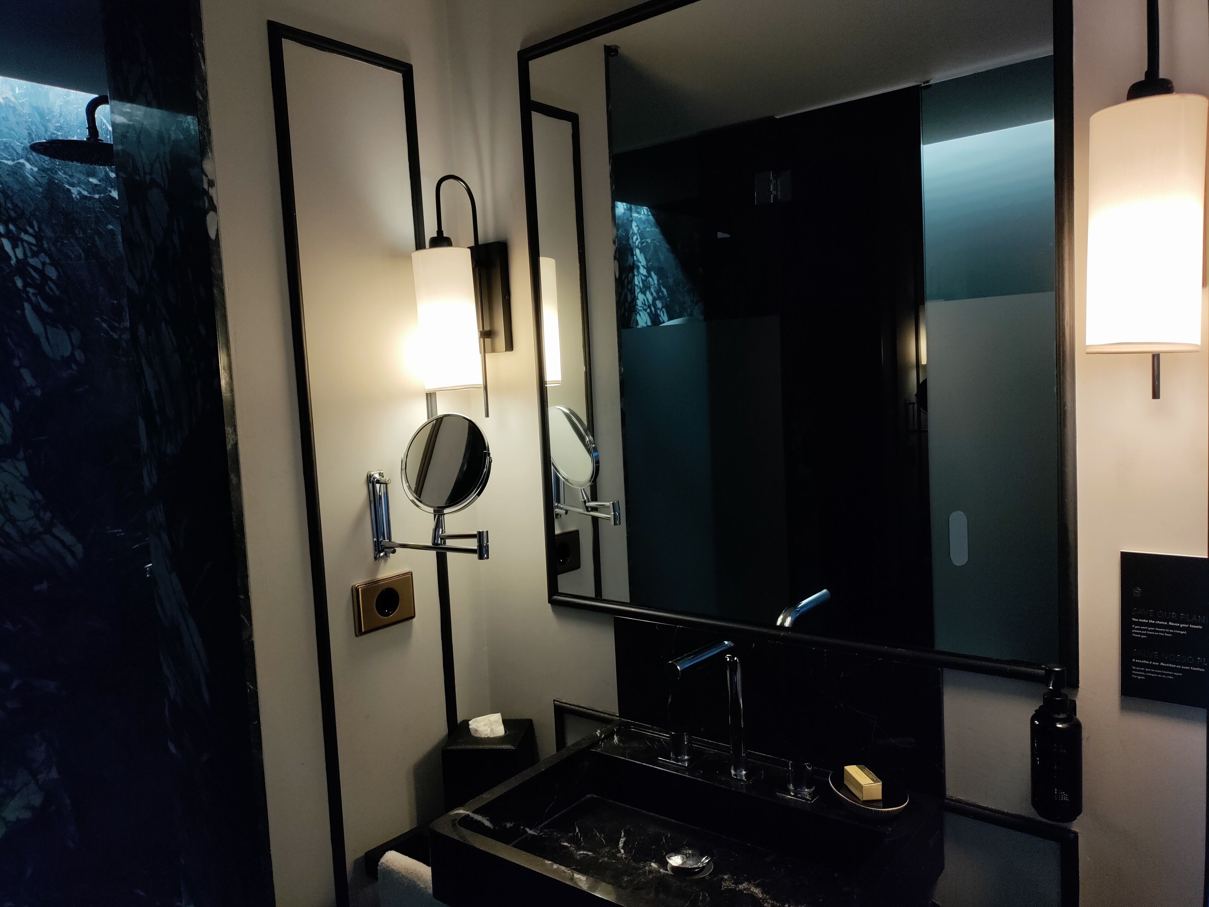 Une salle de bain moderne avec un lavabo noir, un grand miroir et un luminaire fixé au mur.