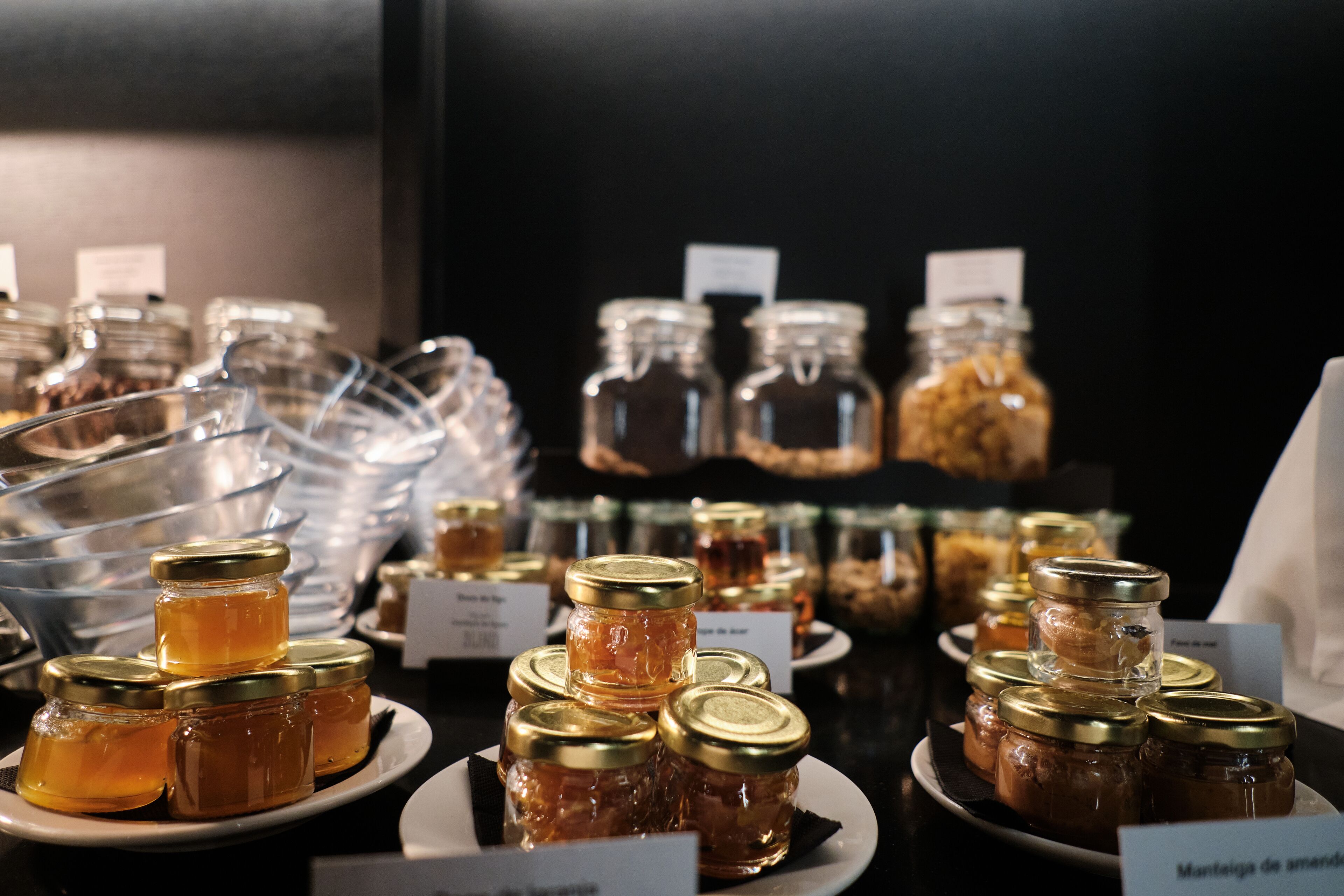 A display of various jars of honey on plates with labels, likely in a store or cafe setting.
