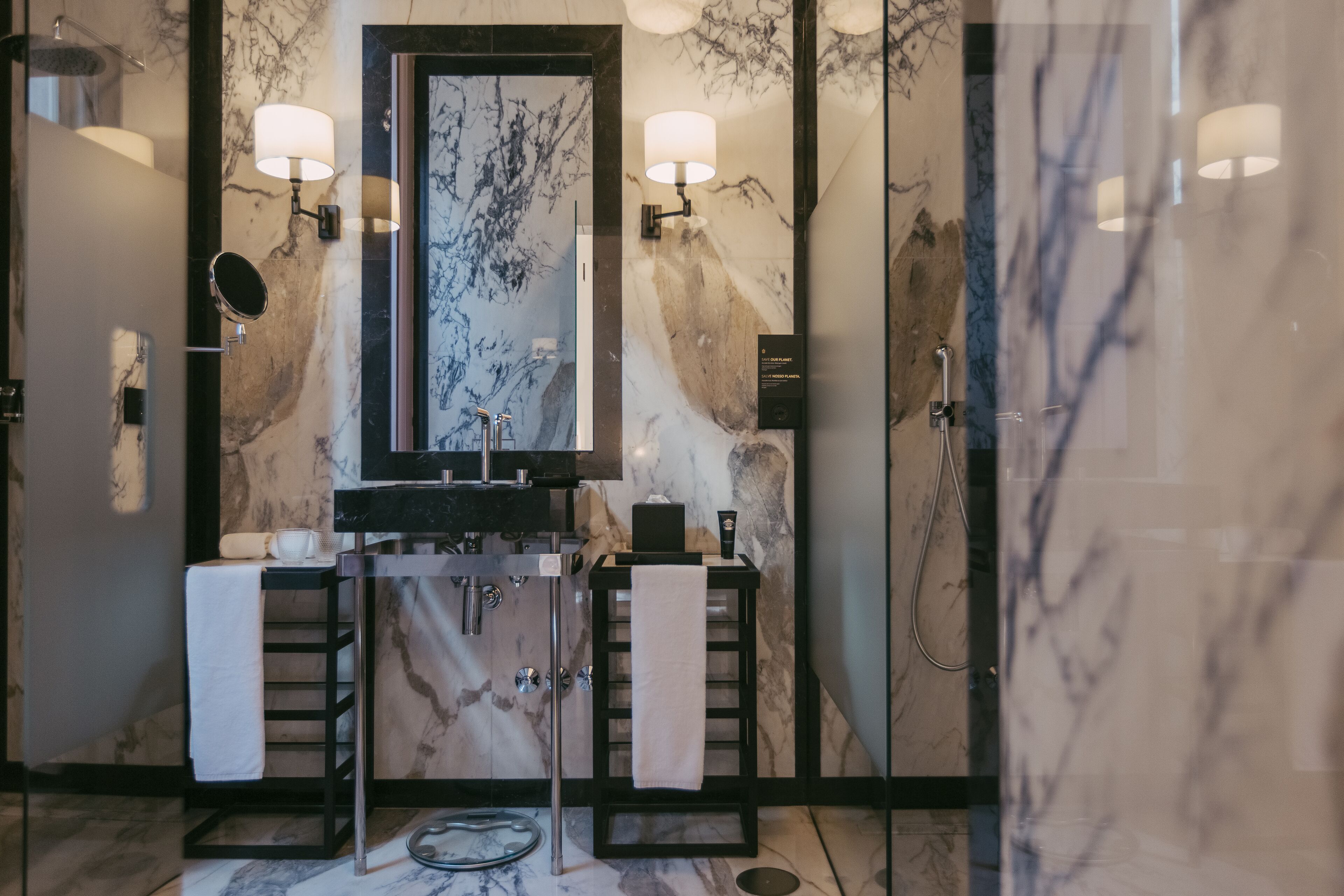 A modern bathroom with a marble vanity, two towel racks, a large mirror, and wall-mounted lighting.