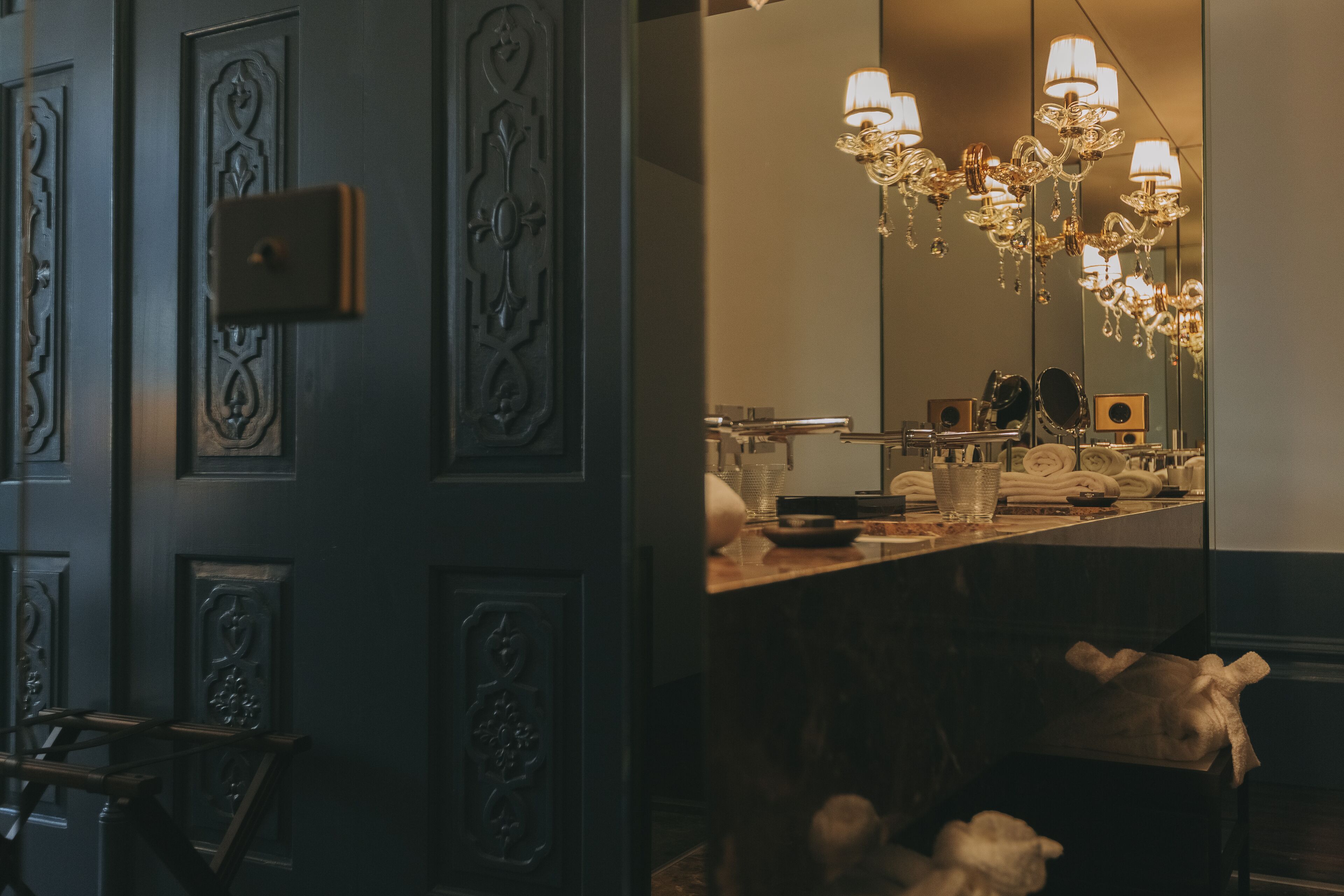 A bathroom with a mirror, a chandelier, and a towel rack.