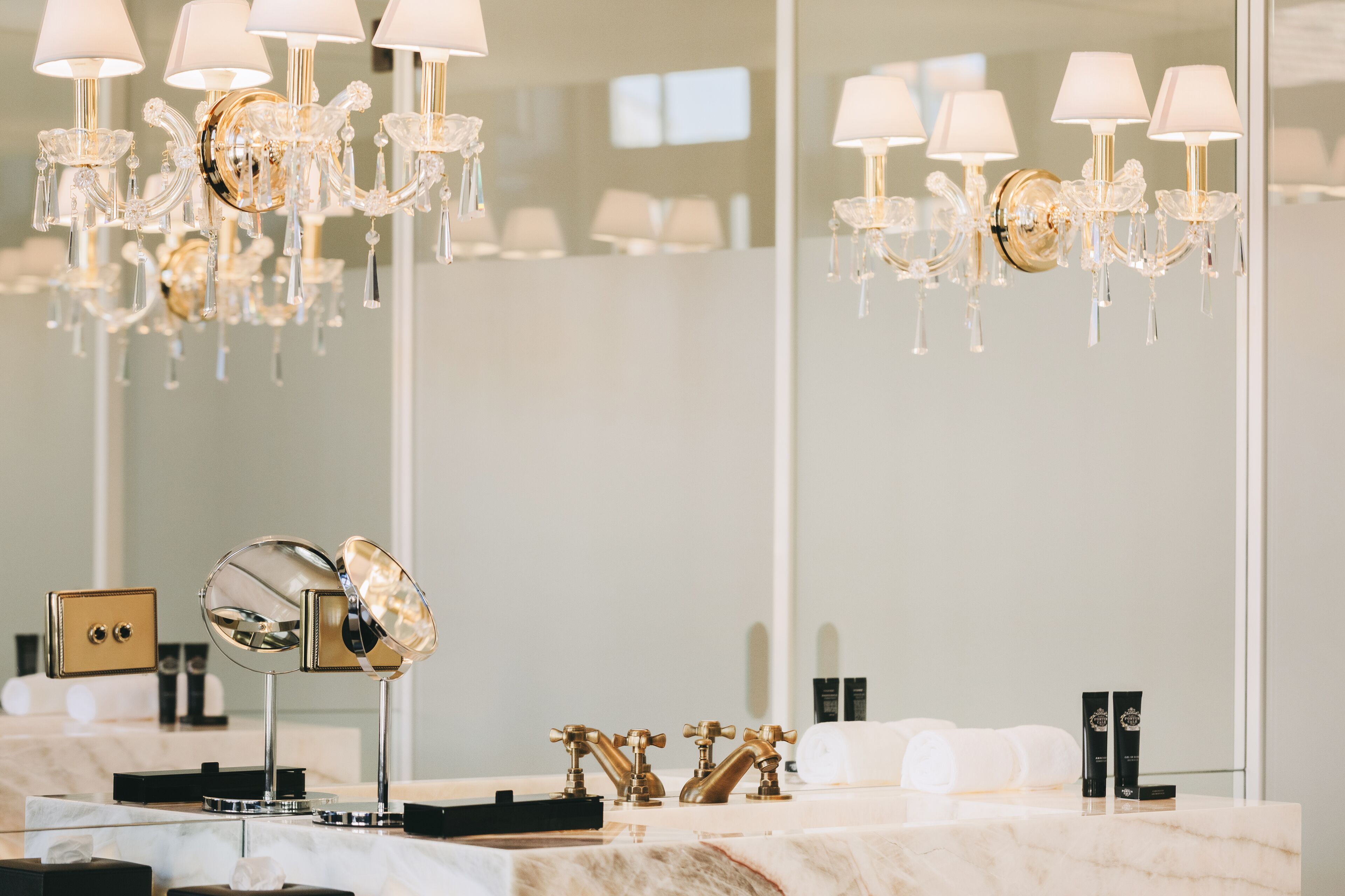 A bathroom with a marble countertop, a gold faucet, a mirror, and a chandelier.