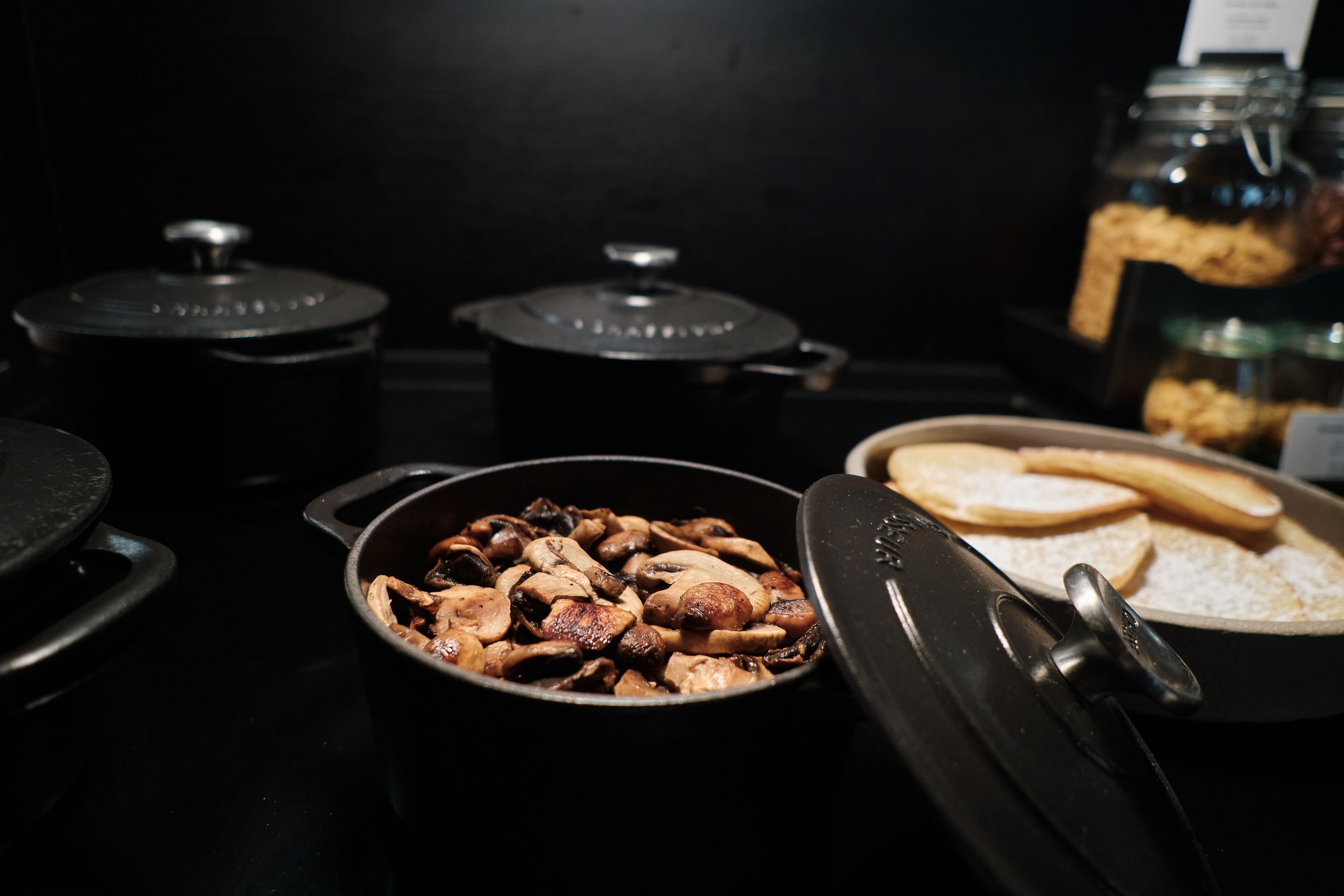 Una cocina con una sartén de setas, una olla con tapa y un plato con pan y una galleta.