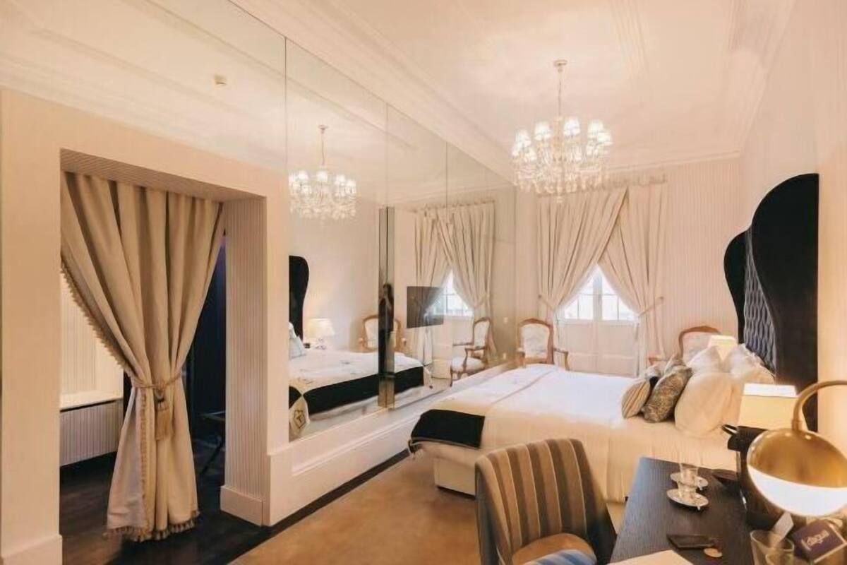Une chambre d’hôtel avec un lit, un bureau, une chaise, un miroir et un lustre.