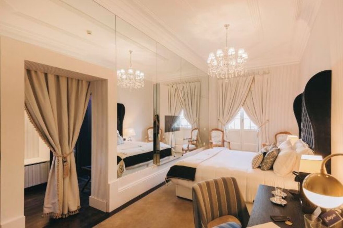 Quarto de hotel com cama, escrivaninha, cadeira, espelho e lustre.