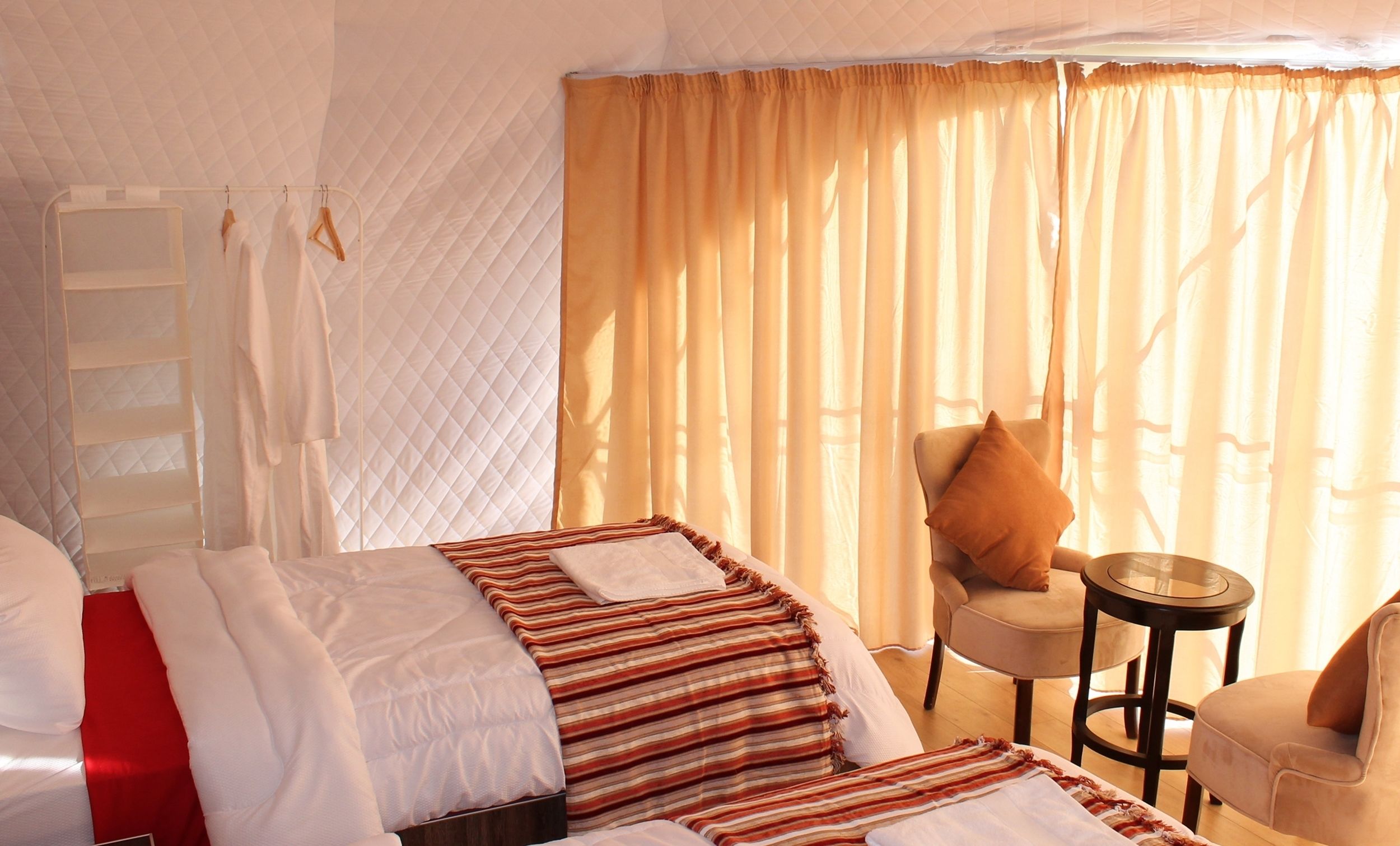 A hotel room with a bed, a chair, a small table, and a window with curtains.