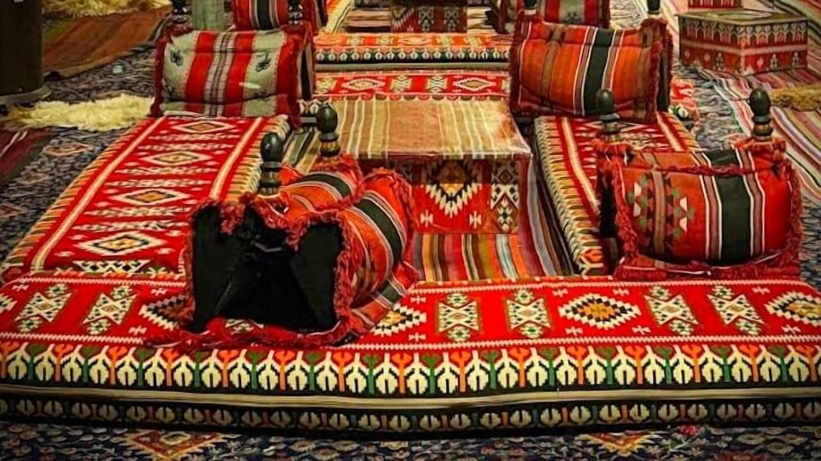 A room with a central area covered by a patterned rug, surrounded by sofas and cushions with traditional designs.
