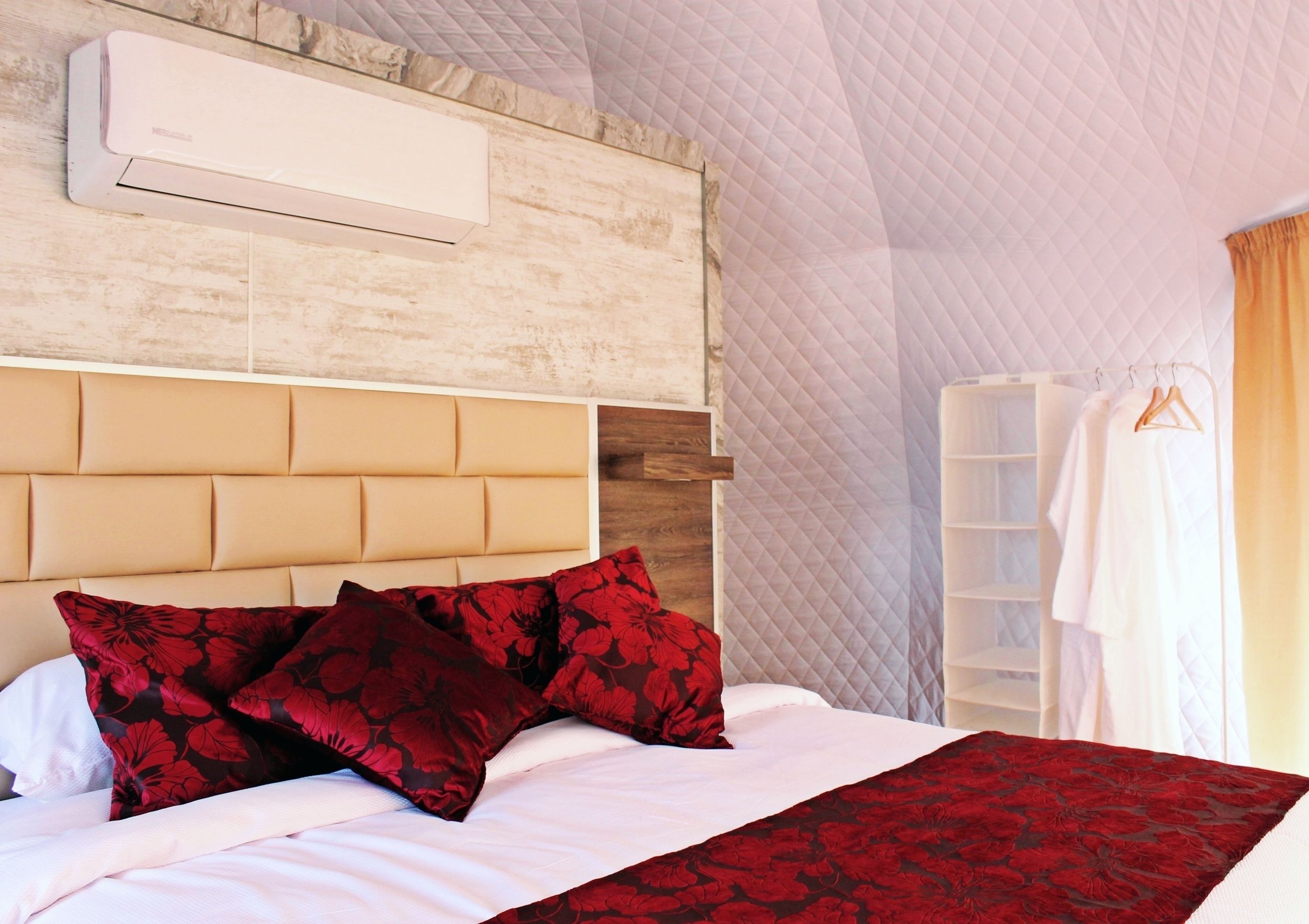 A hotel room with a bed, a headboard, a wardrobe, and a wall-mounted air conditioner.