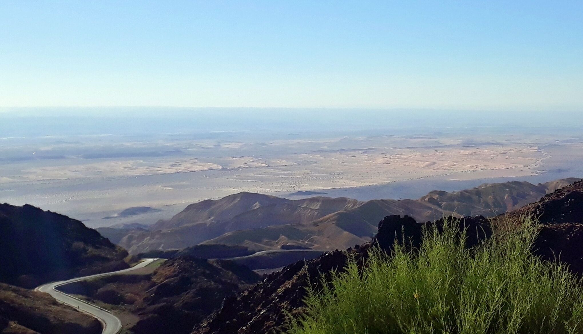 Paisaje montañoso con una carretera serpenteante y una vista distante de una ciudad.