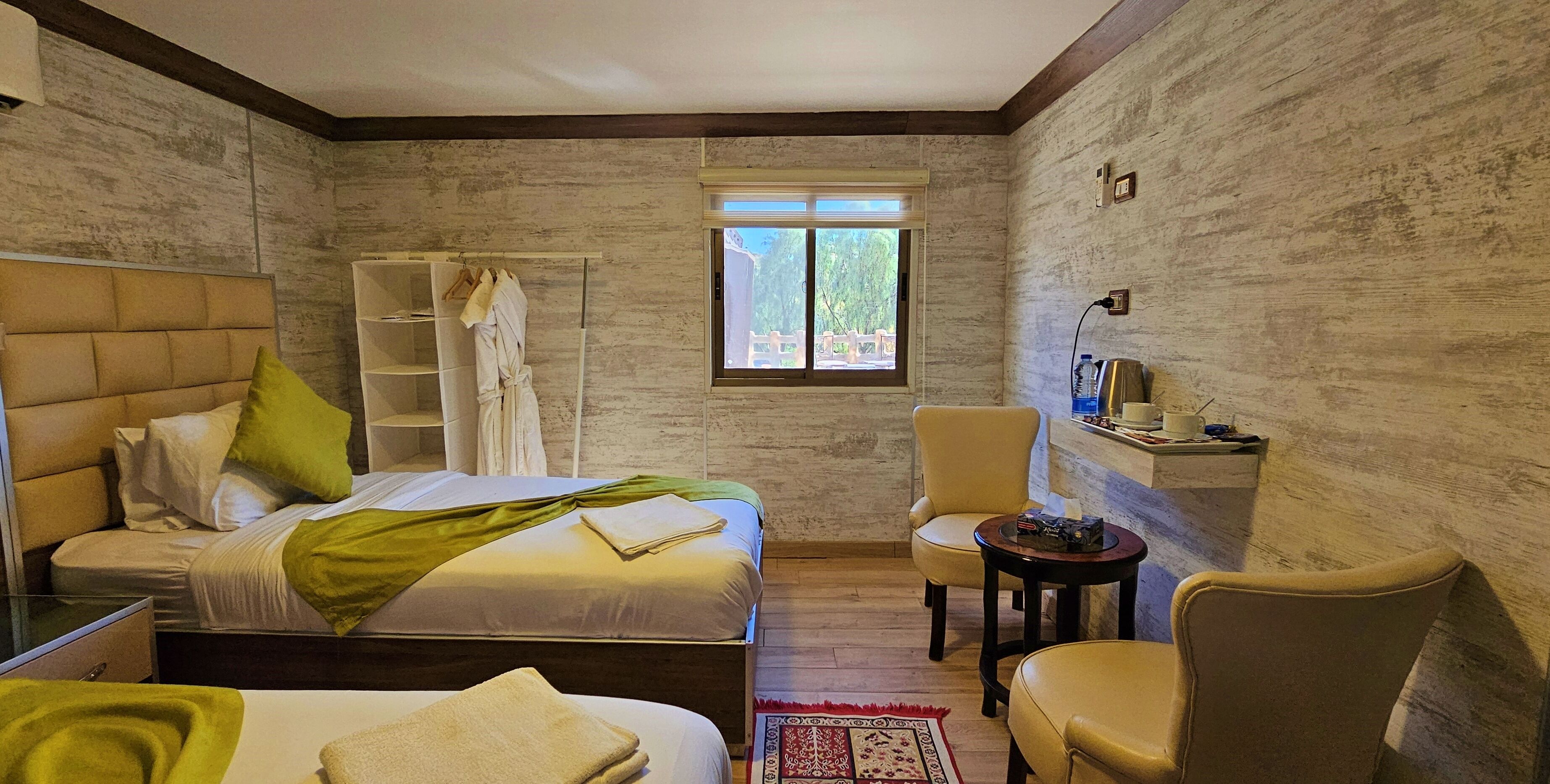 A hotel room with a bed, a chair, a small table, a window, and a wardrobe.