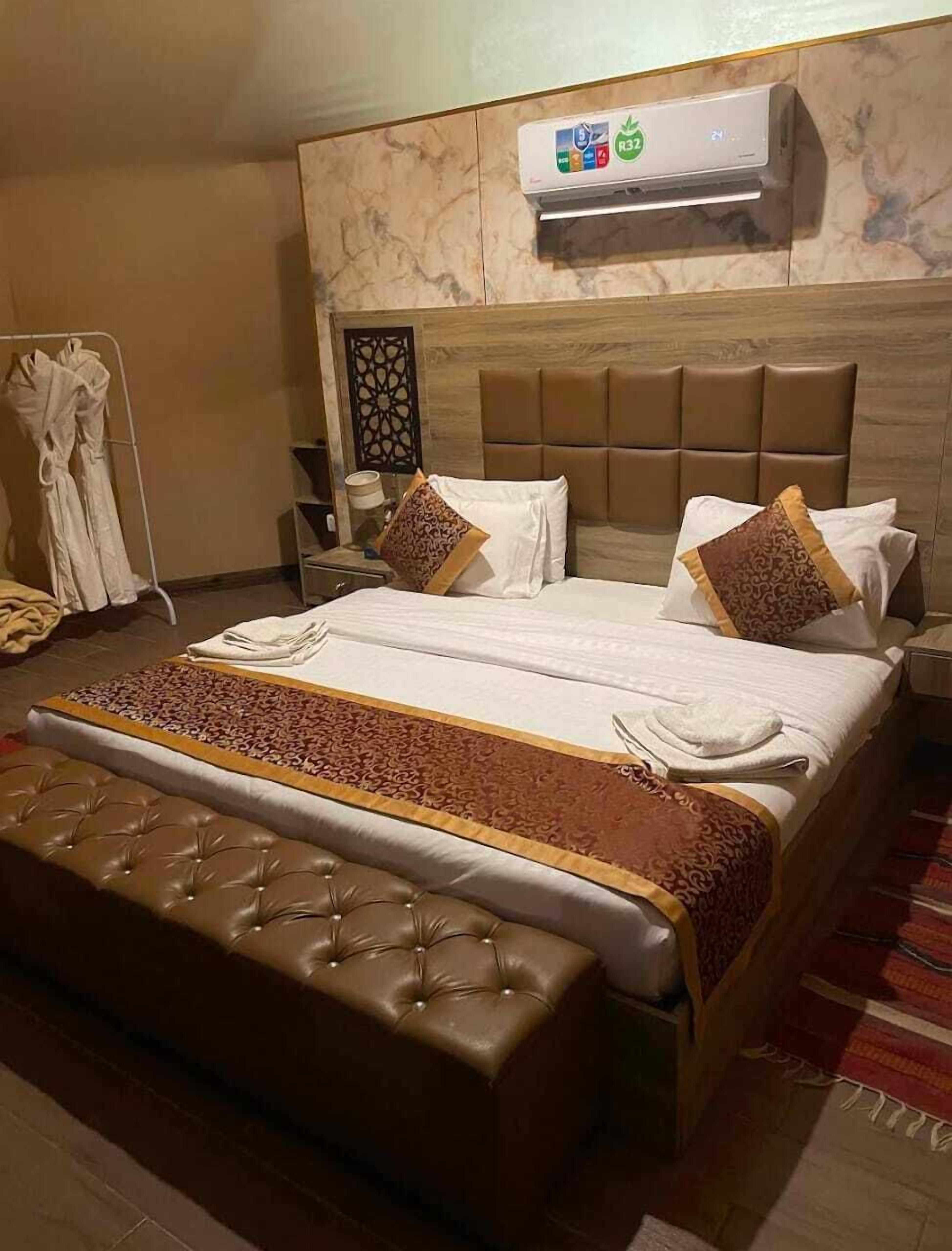 Habitación de hotel con una cama grande, cabecera, mesita de noche, perchero para bata y equipo de aire acondicionado.