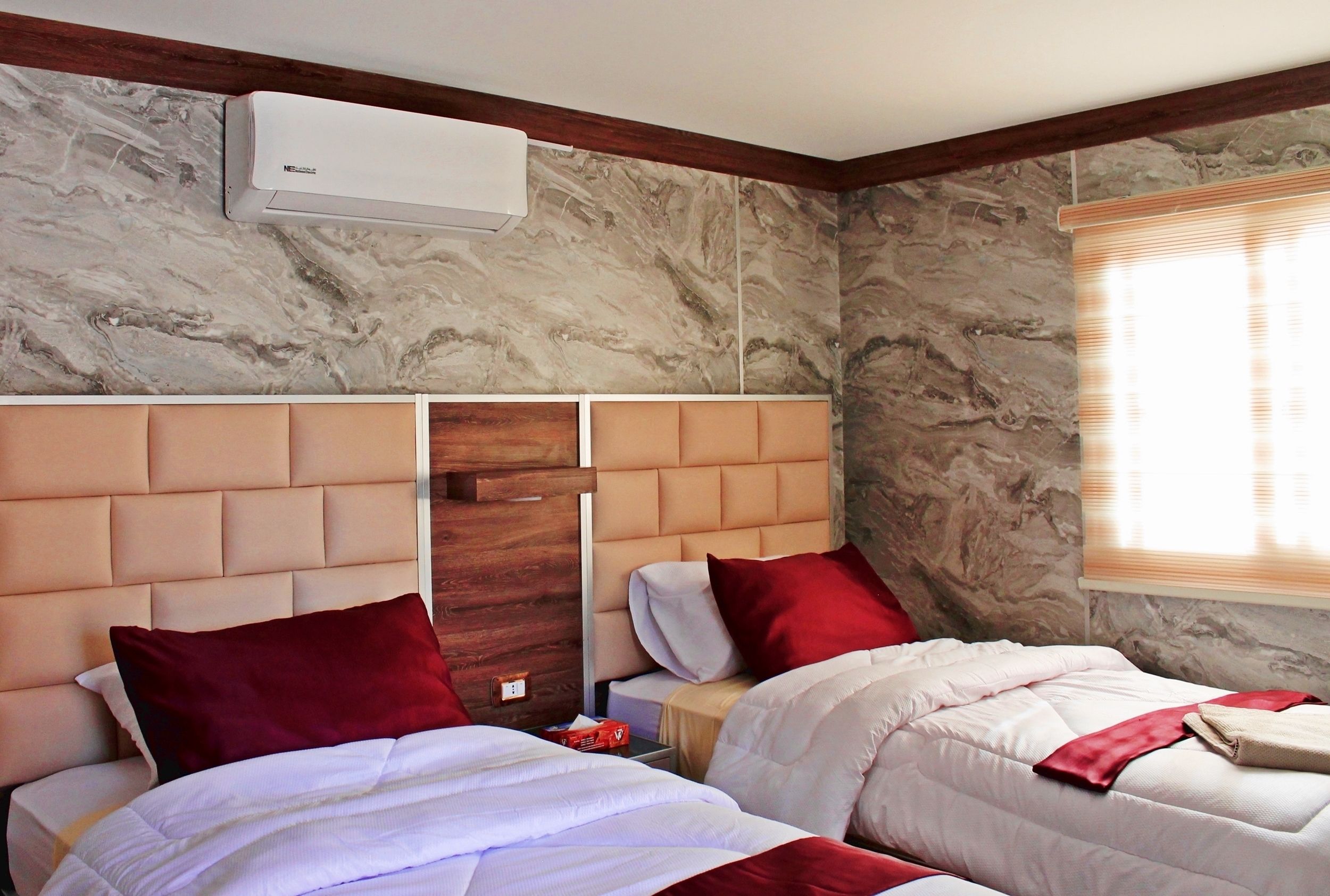 Habitación de hotel con dos camas, paredes de mármol, cabecero de madera y un equipo de aire acondicionado.