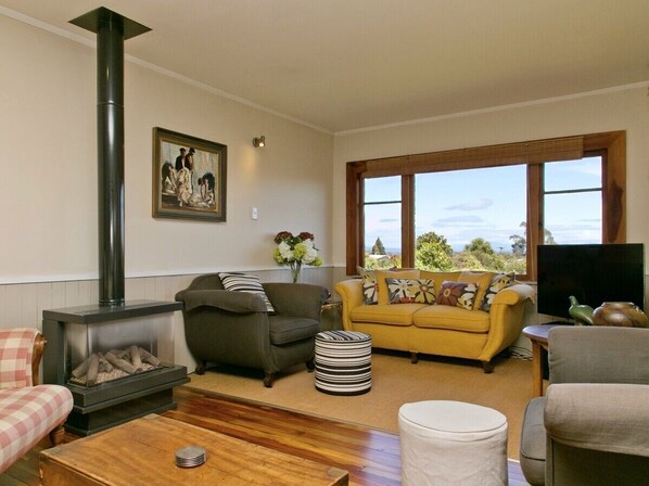Un salón acogedor con chimenea, un sofá, un sillón amarillo y una televisión.