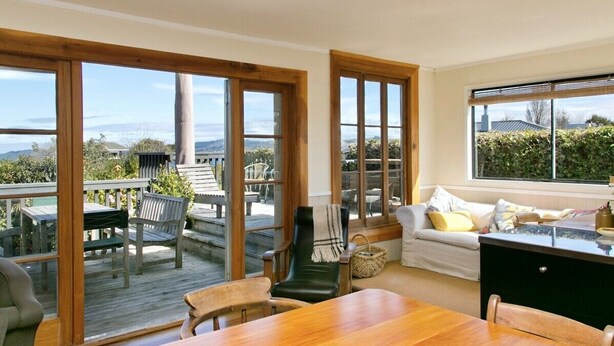 A spacious living area with a wooden dining table, a sofa, and a large window overlooking a deck.