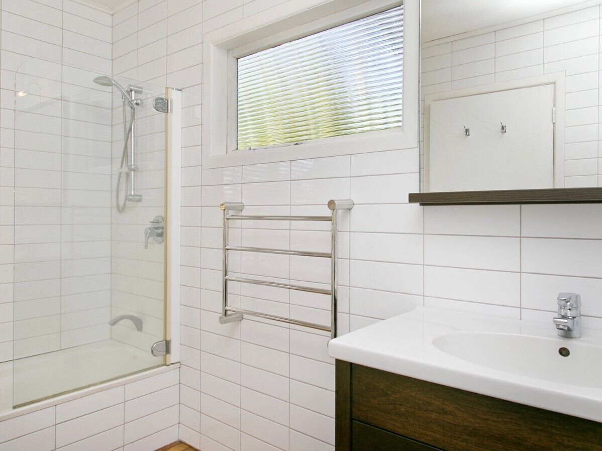 Une salle de bain avec une douche en verre, un porte-serviettes, un lavabo avec un miroir et une fenêtre avec des stores.