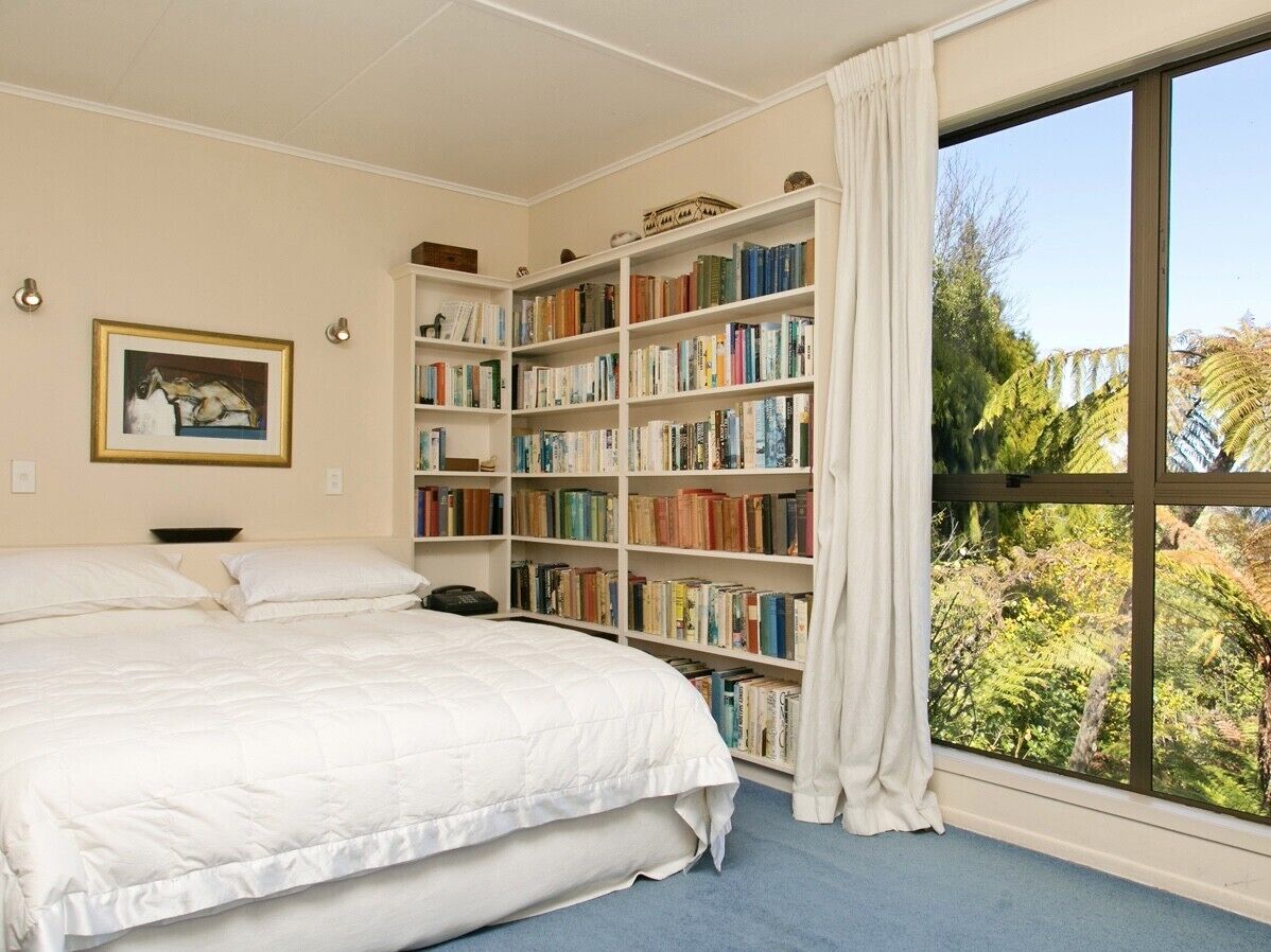 Ein Schlafzimmer mit einem großen Bett, einem Bücherregal und einem Fenster mit Blick auf Bäume.