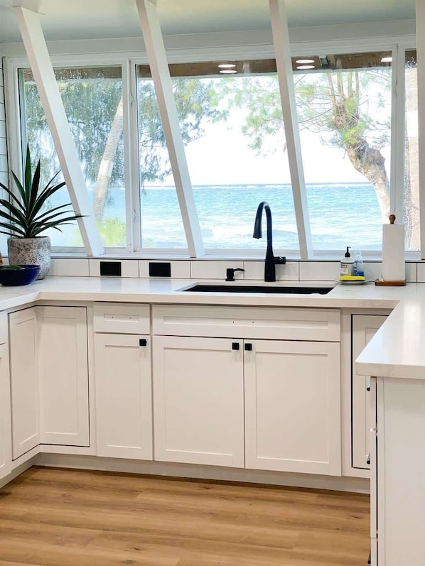 A kitchen with white cabinets, a black sink, and a view of the sea through large windows.