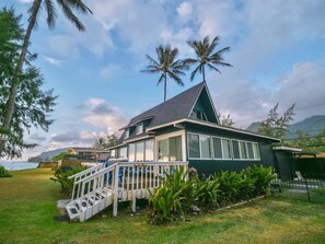 A house with a balcony, surrounded by greenery and palm trees.