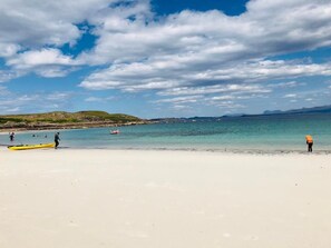 Une plage avec un ciel dégagé, une eau calme et des collines qui se dessinent à l’horizon.