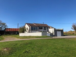 Une maison à deux étages avec un toit en pente, un porche à l’avant et un petit garage attenant.