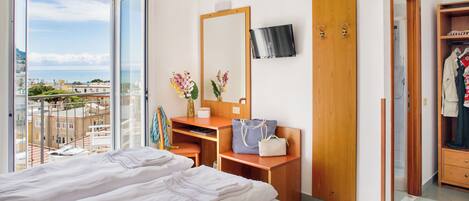 Habitación de hotel con una cama grande, un escritorio con espejo, un televisor montado en la pared y vistas de la ciudad a través de un ventanal.