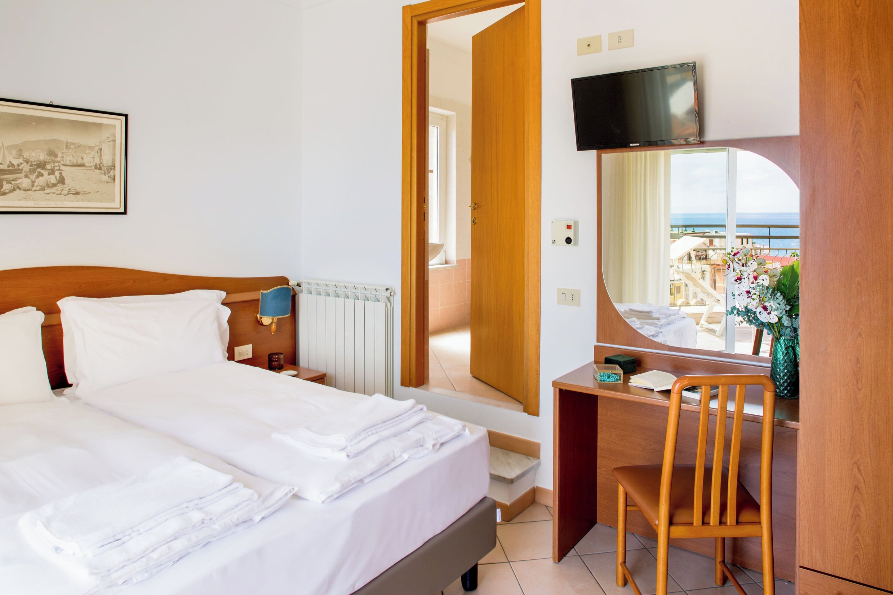 Habitación de hotel con cama, escritorio, silla, televisor y vista al mar.