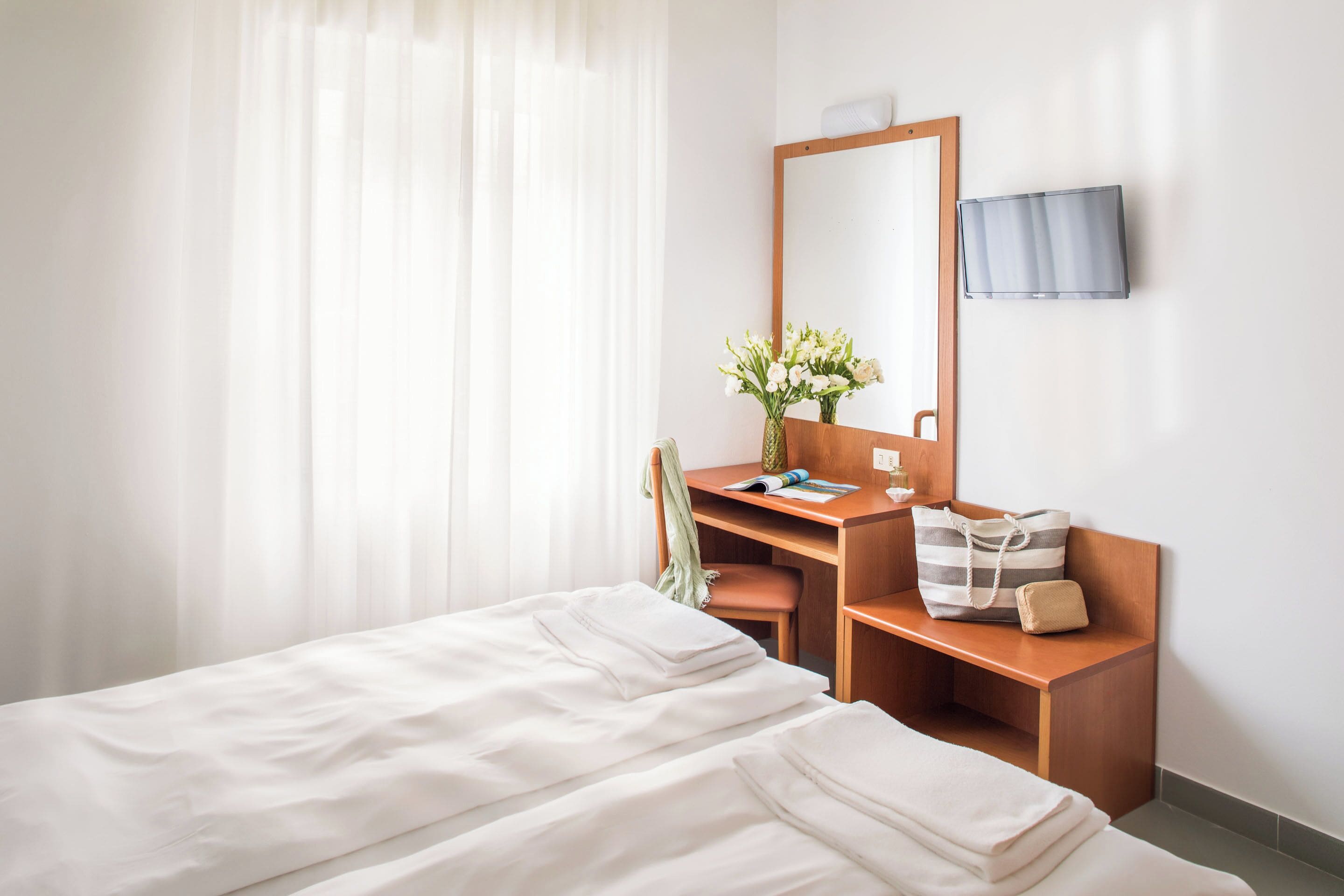Ein Hotelzimmer mit einem Bett, einem Schreibtisch, einem Sessel, einem Spiegel, einem Fernseher und einem Fenster mit Vorhängen.