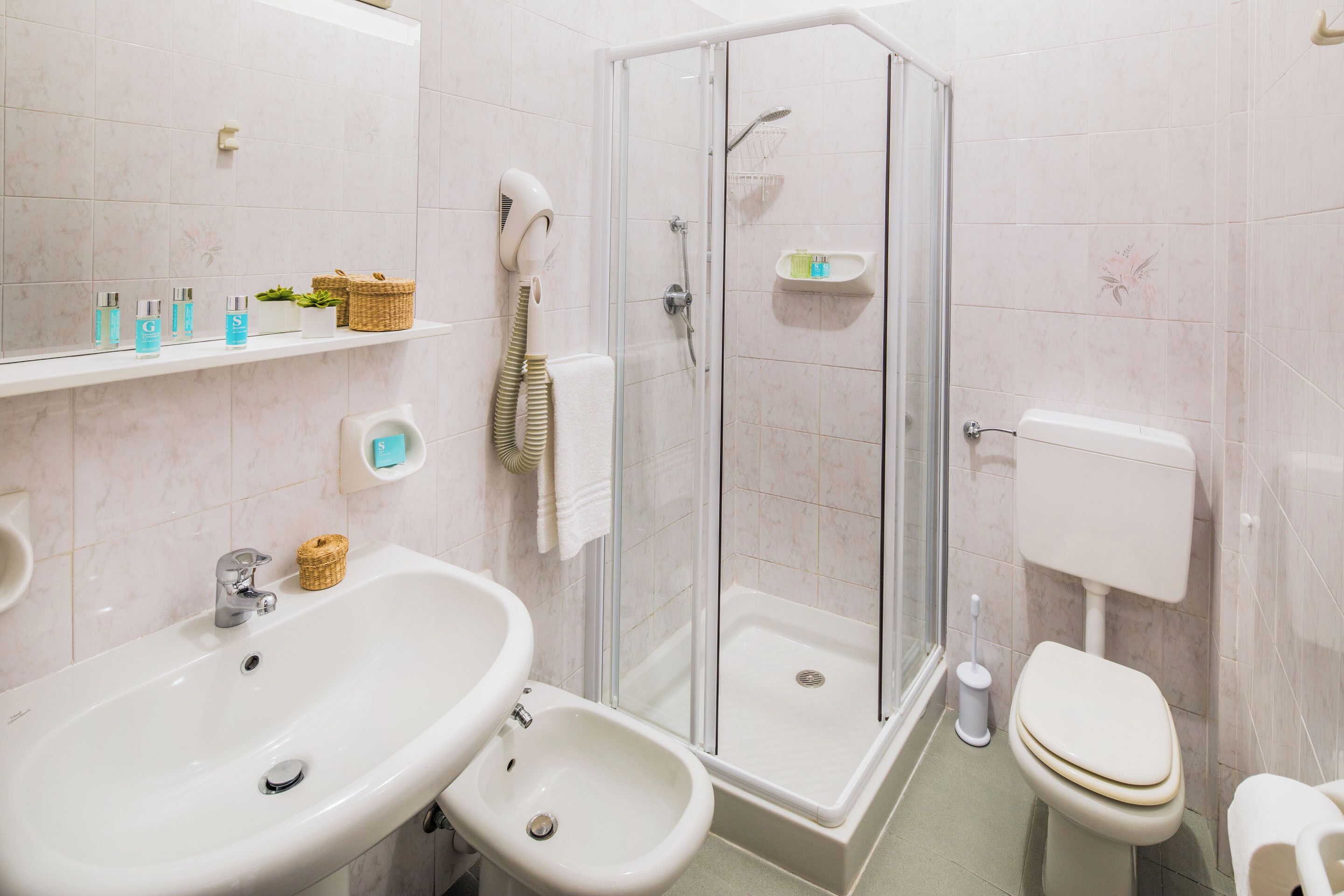 Ein modernes Badezimmer mit einer gläsernen Duschkabine, einem Waschbecken mit Bidet, einer Toilette und einem Ablagefach für Toilettenartikel.