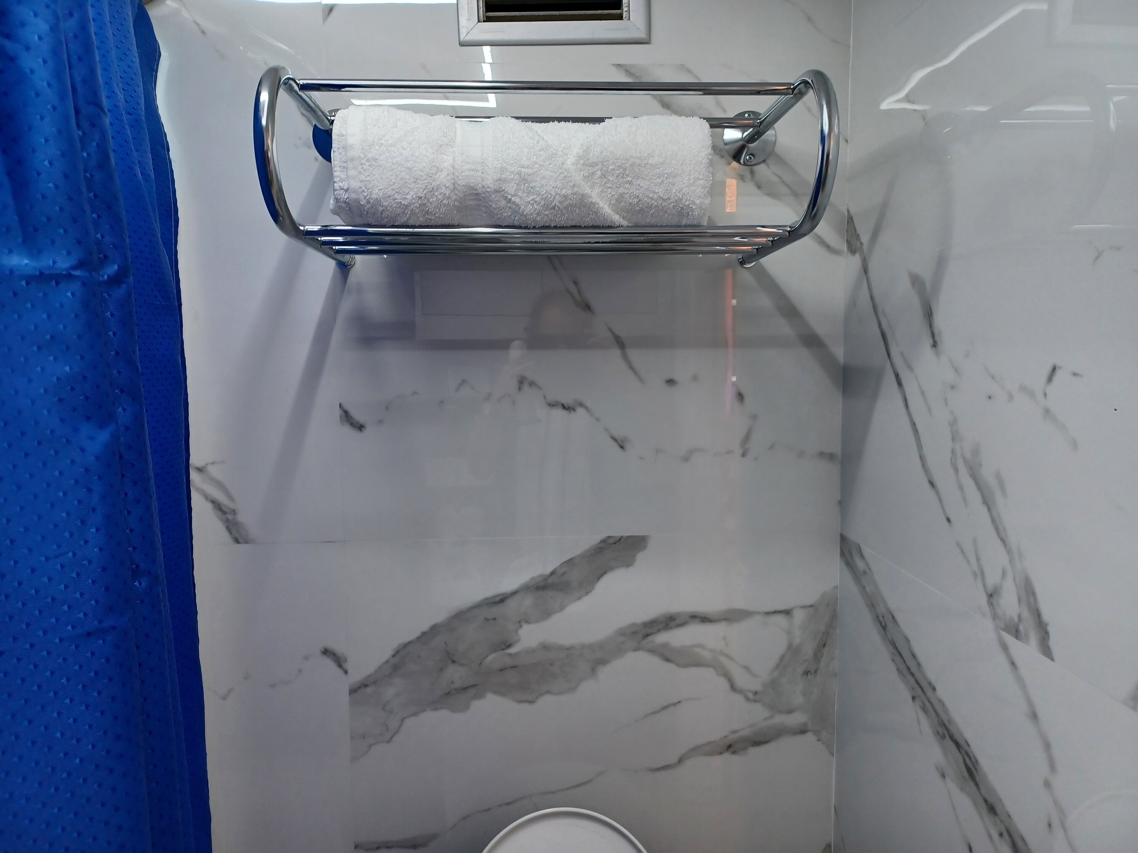 Une salle de bain avec un mur en marbre, un porte-serviettes sur lequel est posée une serviette blanche, et un rideau de douche bleu.