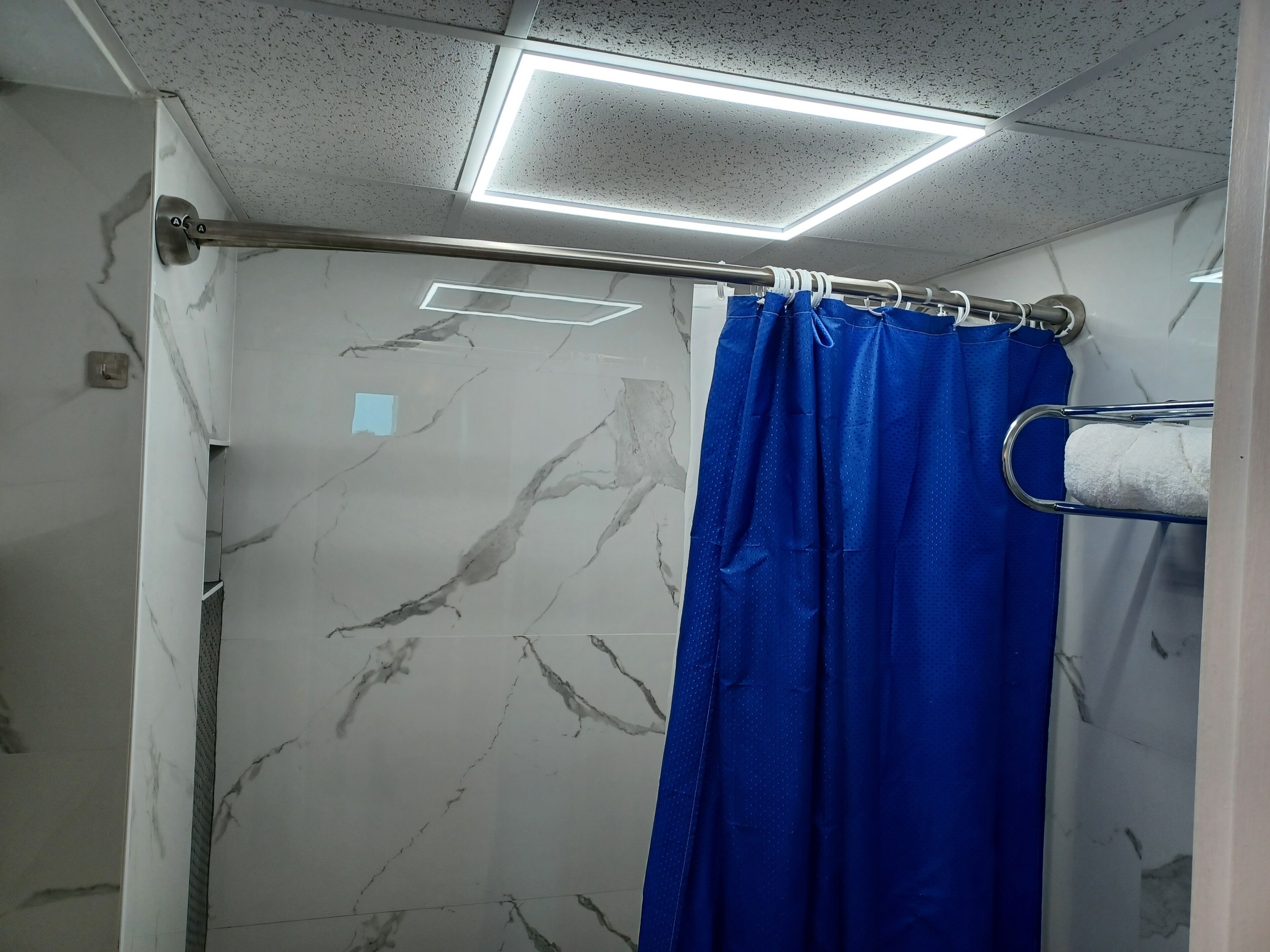 Une salle de bain avec un rideau de douche, un porte-serviettes et des murs en marbre.