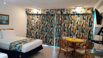 A hotel room with a bed, a dining table with chairs, a TV, and curtains with a tropical pattern.