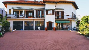 A two-story building with a tiled roof, multiple balconies with potted plants, and a paved driveway. - Casa Marina .. a stone's throw from the center! (Verbania)