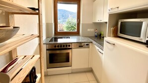 Eine kompakte Küche mit weißen Schränken, einem eingebauten Backofen, einer Mikrowelle und einem Fenster mit Blick auf die Berge.
